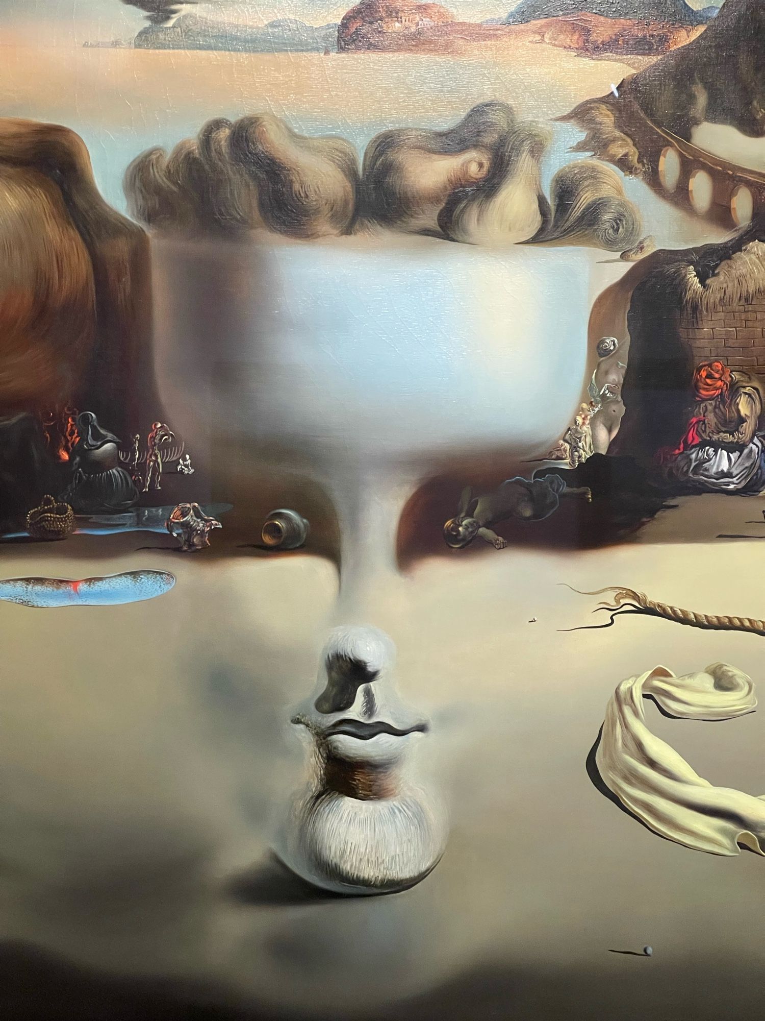 At first glance the spectator sees a desolate beach. As the viewer studies the work, a face appears, then a dish filled with pears, then the profile of a dog. These images are fragmented further as the dog's collar becomes a bridge and his head a hill. The instability of appearances fascinated Dalí, who sought to evoke the world of the unconscious by creating these simultaneous images.
The meticulously painted objects and fragments make the metamorphoses and unexpected juxtapositions of the objects even more startling.