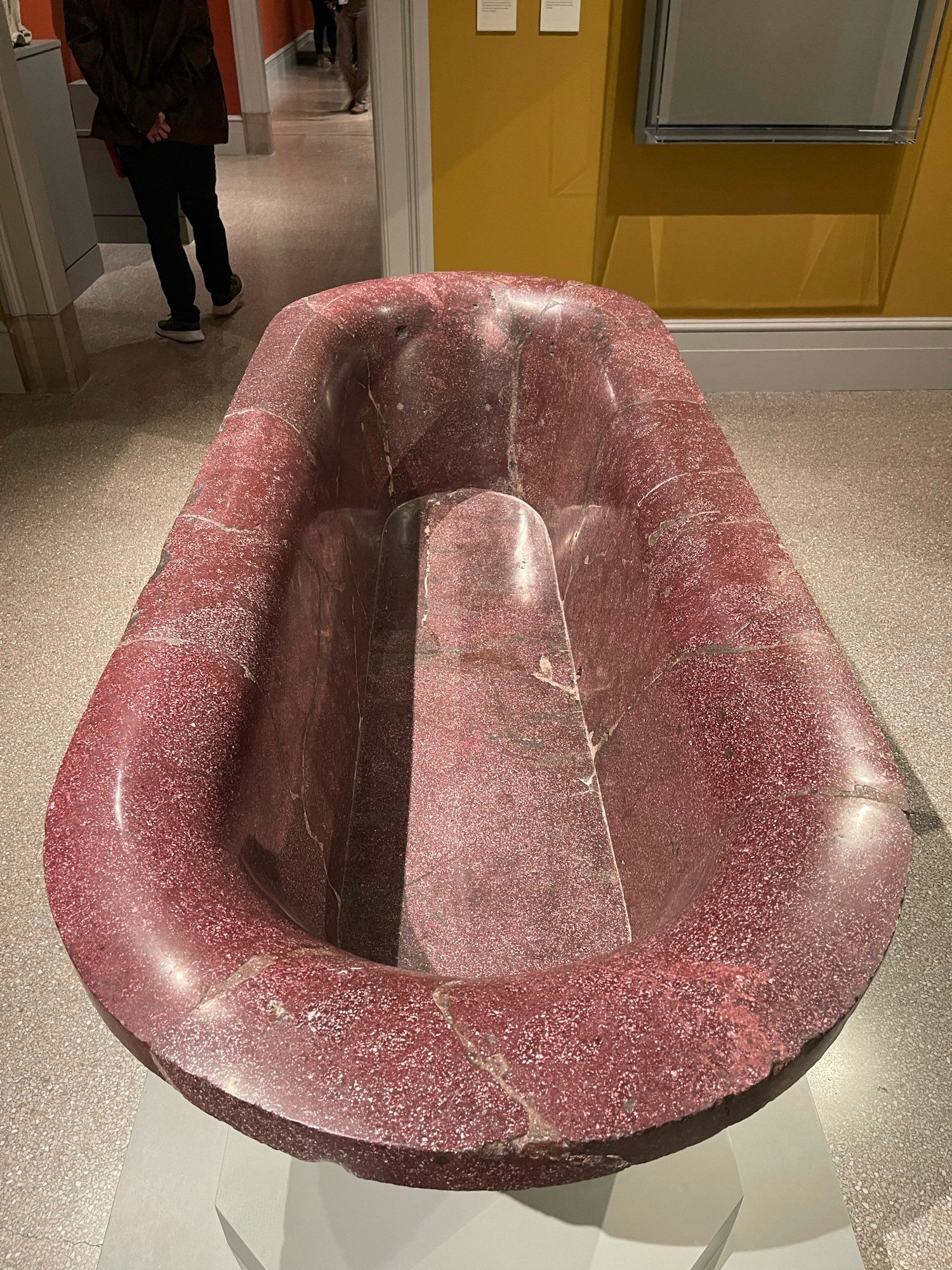 The original function of large stone basins, such as the one in the middle of this gallery, is not yet known. This basin's decorative imagery with stylized ivy leaves and the head of a panther allude to Bacchus, the Roman god of wine, who represented the pleasures of life. The panther's mouth is pierced to function as a drain.
Objects made from the very dense rock called porphyry (meaning purple in Greek) were highly valued since Roman times. In the Byzantine period, these prized goods were frequently relocated and reused. The basins often found new homes as elements in fountains or, after Rome adopted Christianity in the fourth century, were converted to baptismal fonts or sarcophagi.