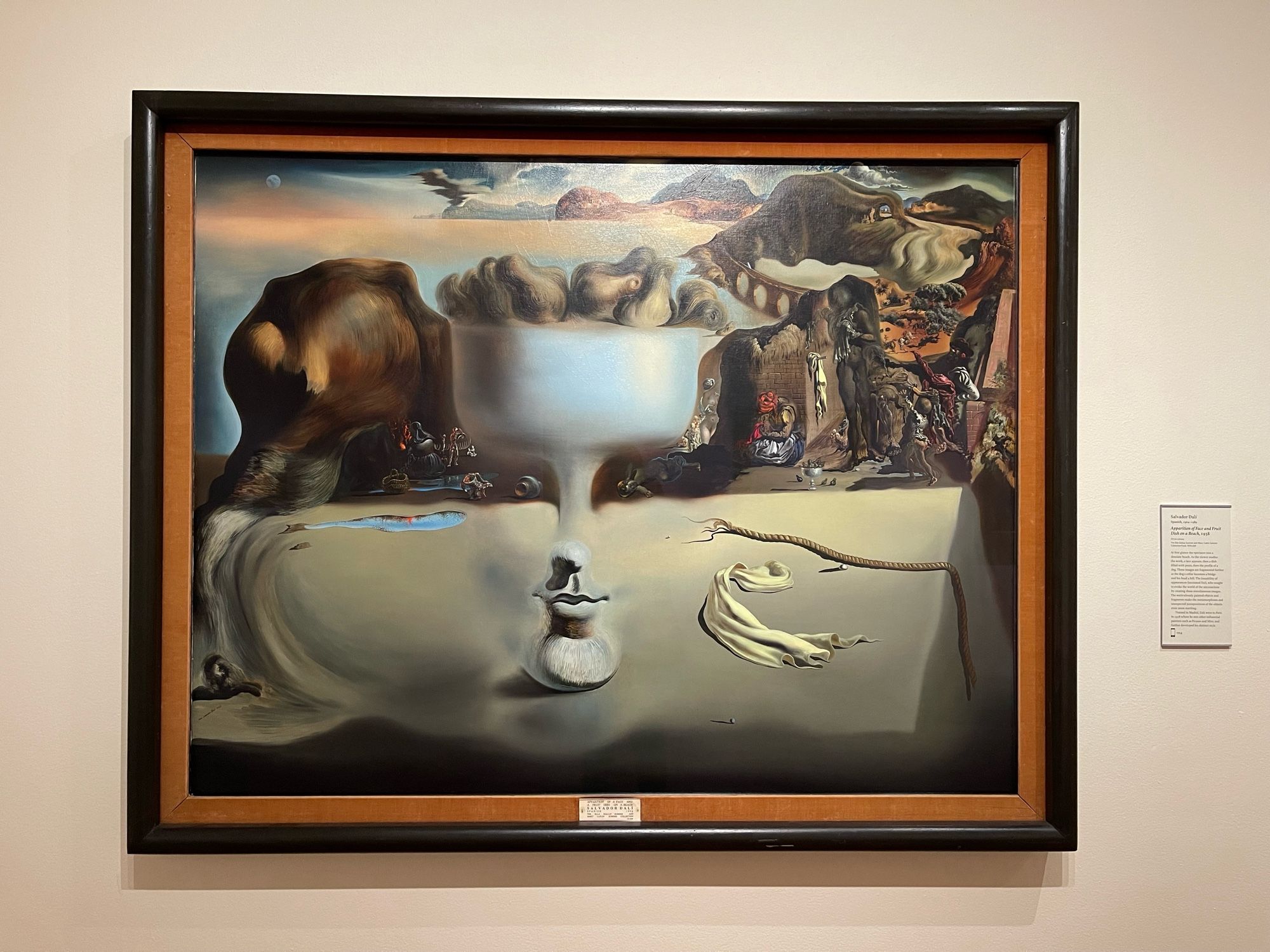 At first glance the spectator sees a desolate beach. As the viewer studies the work, a face appears, then a dish filled with pears, then the profile of a dog. These images are fragmented further as the dog's collar becomes a bridge and his head a hill. The instability of appearances fascinated Dalí, who sought to evoke the world of the unconscious by creating these simultaneous images.
The meticulously painted objects and fragments make the metamorphoses and unexpected juxtapositions of the objects even more startling.