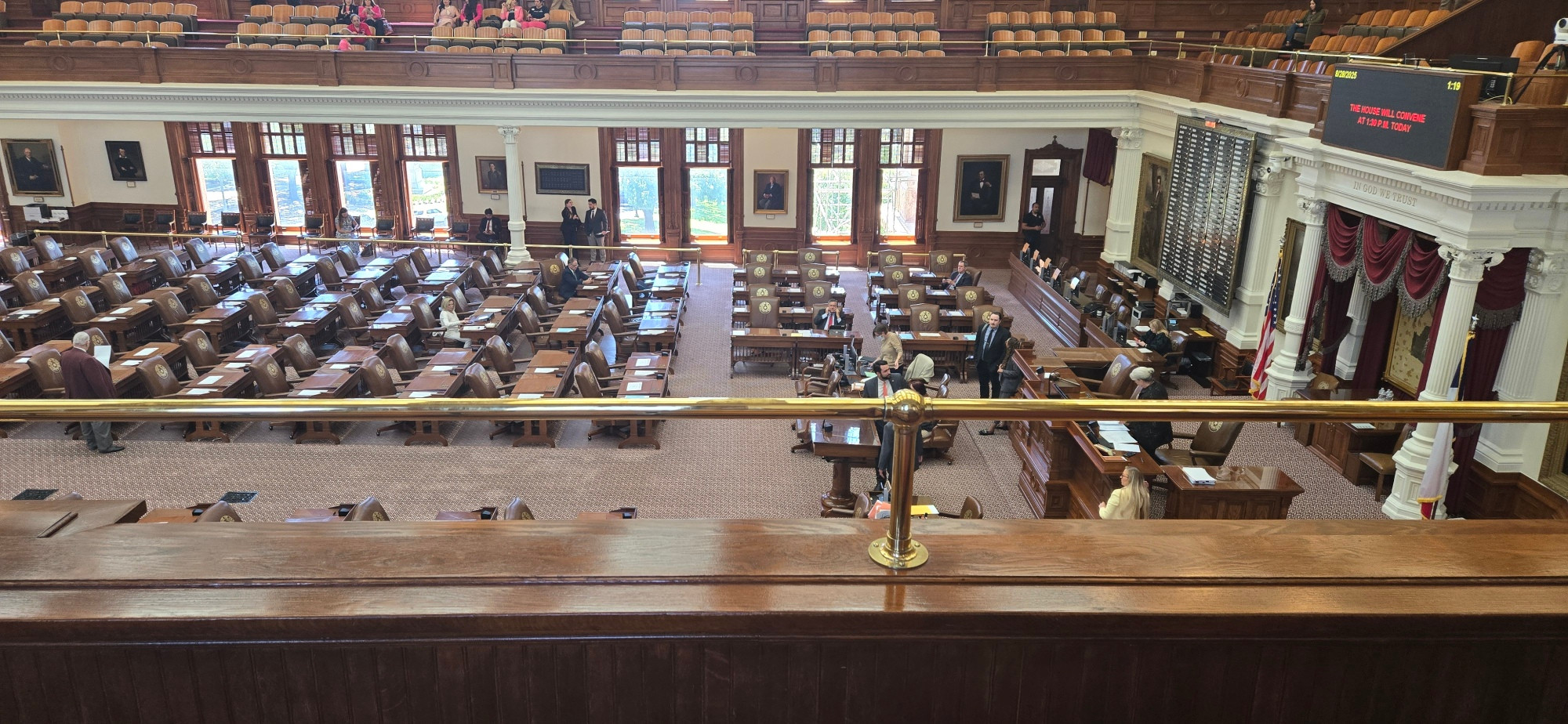 A photo of the Texas House of Representatives, from the gallery. There are lots of brown wooden desks. 