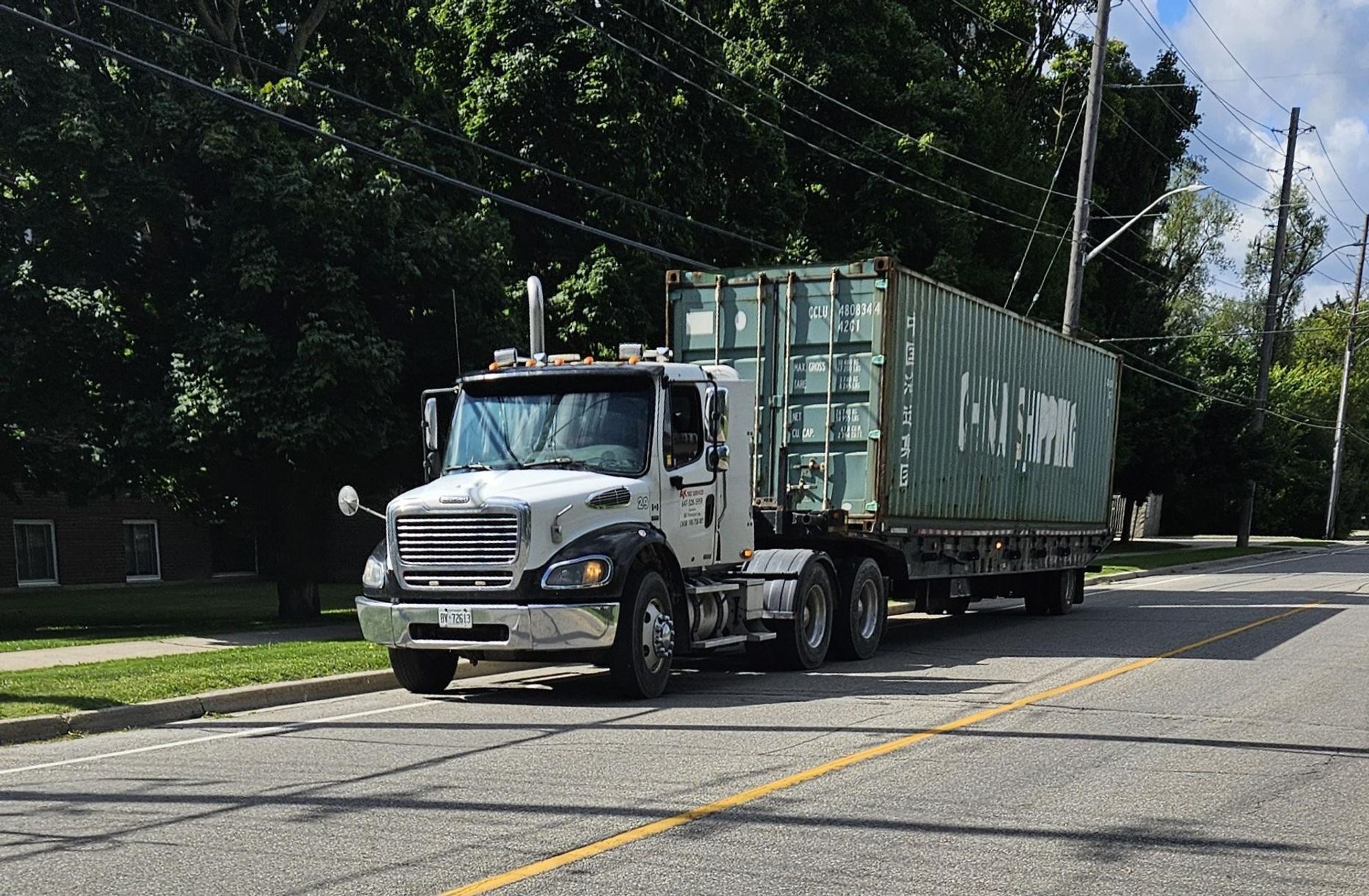 Photo of large transport truck parked in a bike lane. It is hauling a green shipping container that says China Shipping on it.