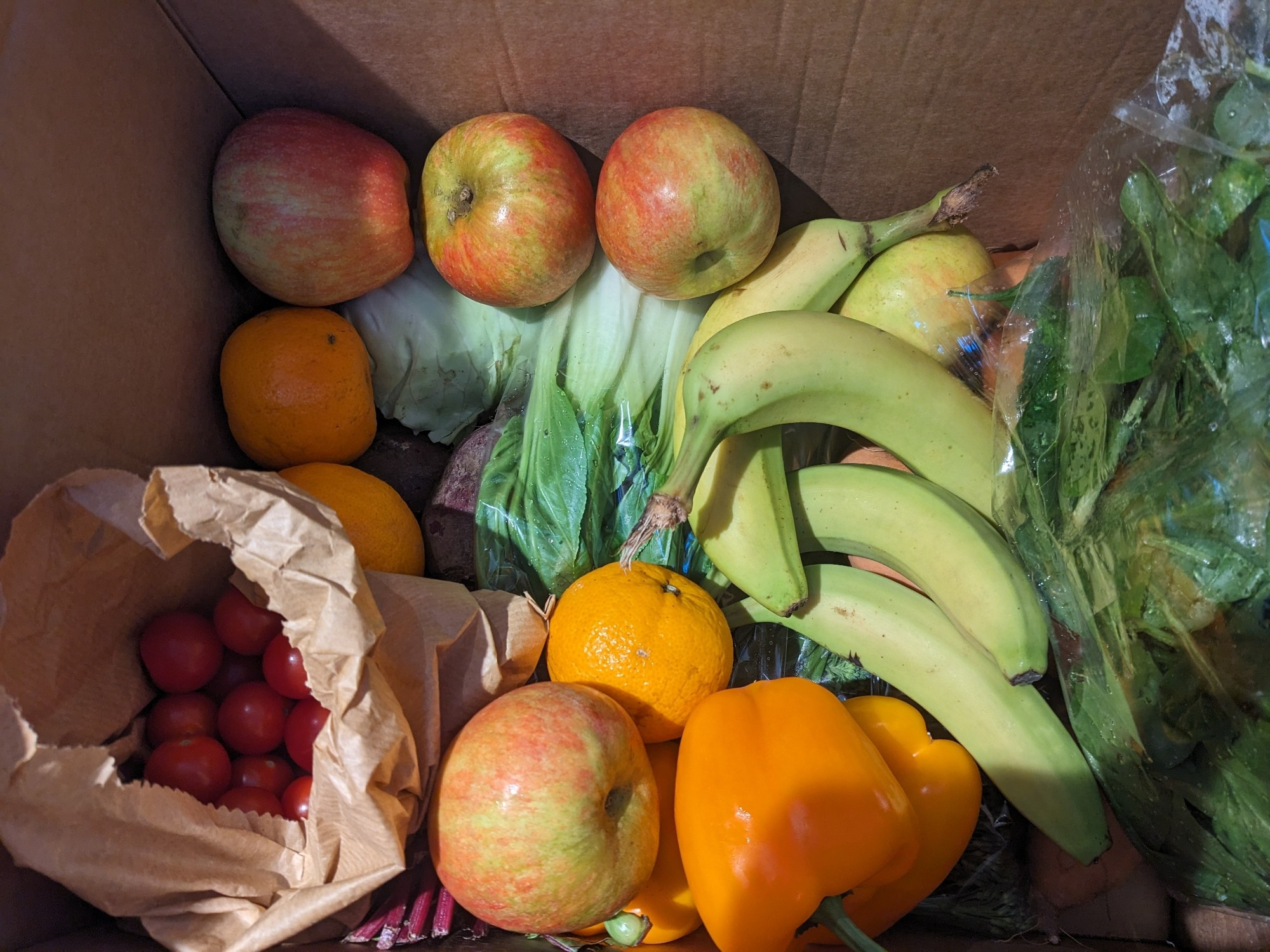 A box of fruit and vegetables, tomatoes, apples, bananas and green veg