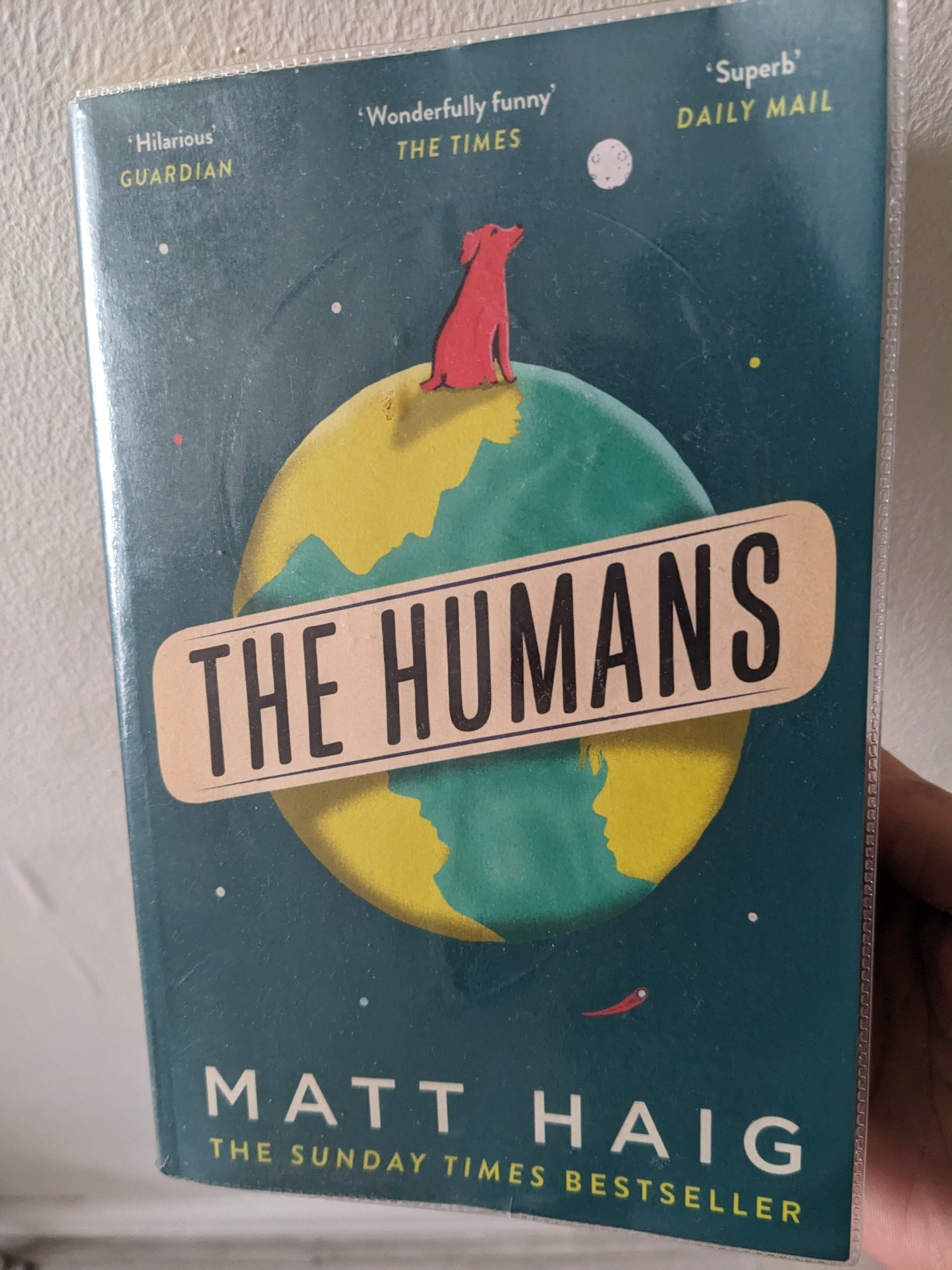 A book called 'The Humans' written by a human called Matt Haig with a planet and a red dog on the cover