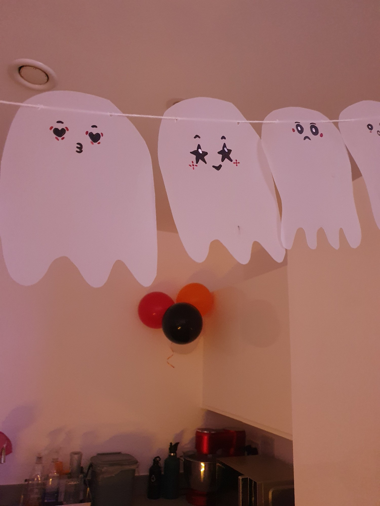 Ghosts cut out of paper with different cute smiley faces, hung on a string like bunting