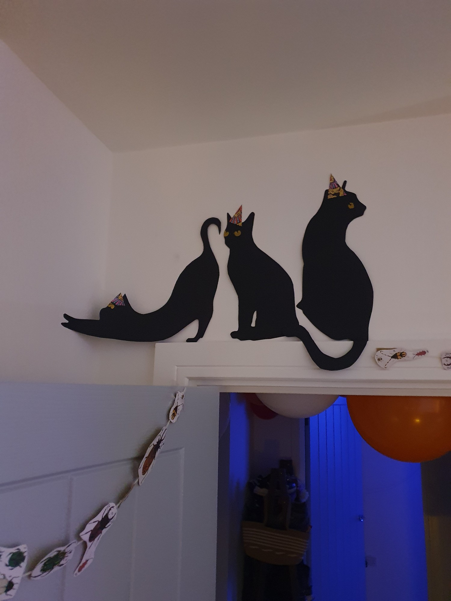 Black cats in leisurely poses stuck to the wall above a doorframe, a trail of paper bugs stuck and draped to the doorframe