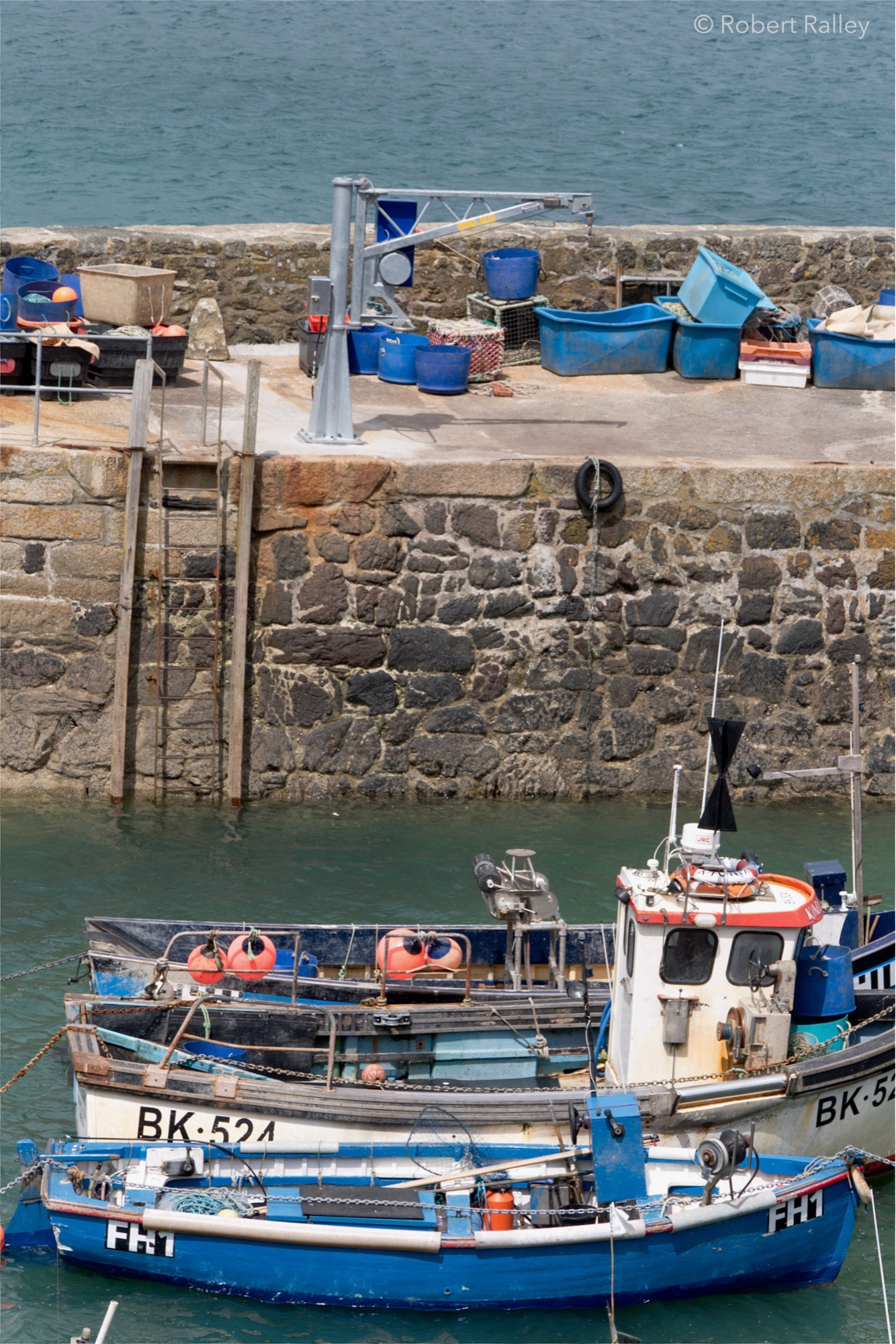 Part of the harbour at Coverack in Cornwall, with three small fishing boats visible, largely coloured blue and white. The nearest of them (fully in shot) has 'FH1' on it and the second (its front out of shot) has 'BK 524'. The third boat is largely hidden behind the other two.