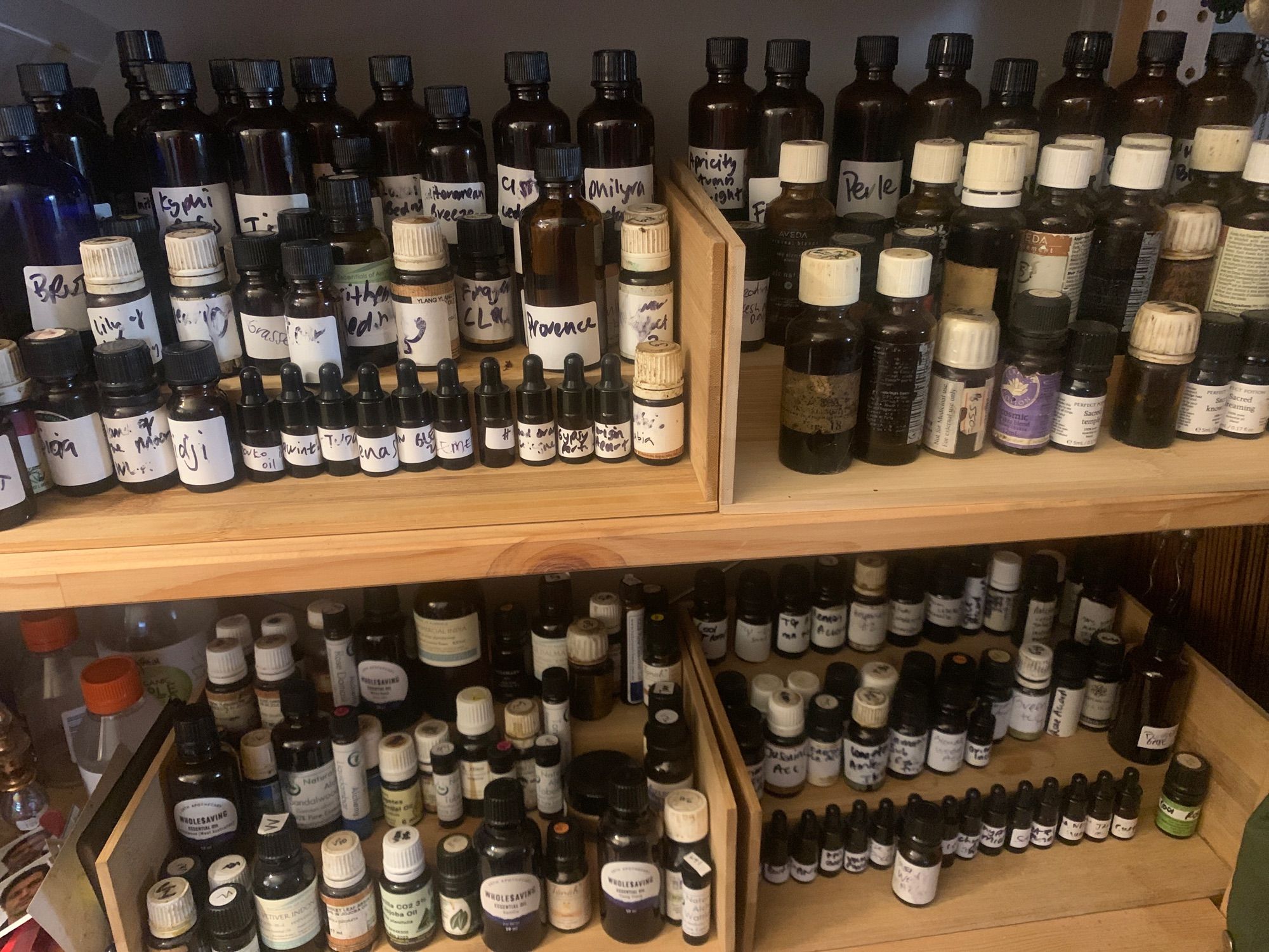 A collection of small brown bottles on bamboo risers on timber shelves. Nearly that all handwritten labels indicating which essential oil perfume mixes records are inside. This is a small part of my collection