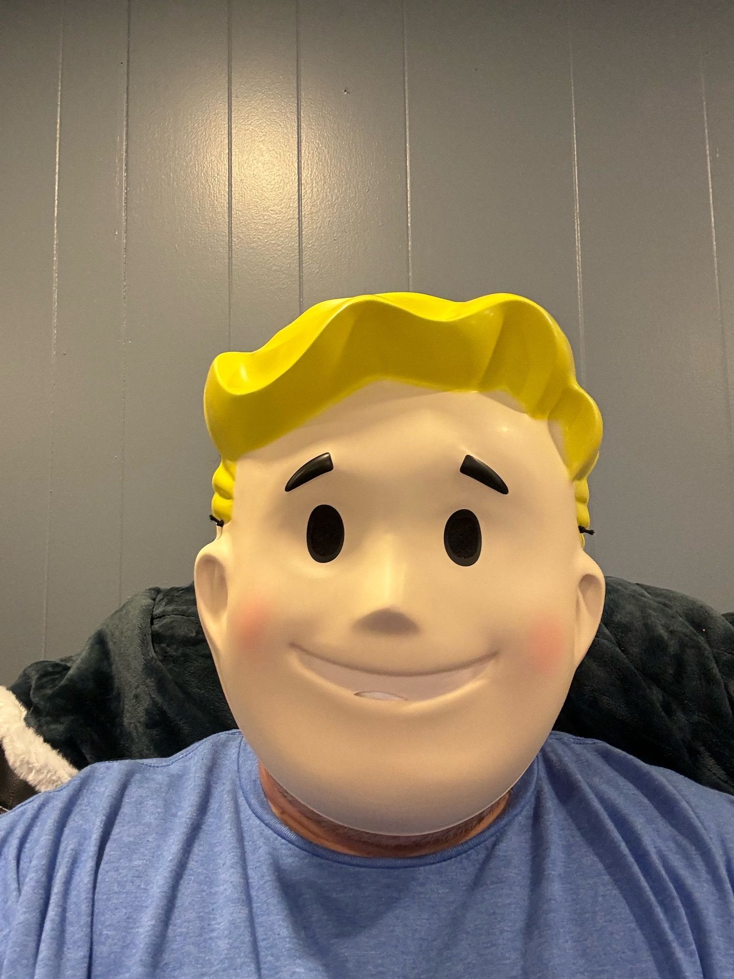 Me in a light blue T-shirt wearing a plastic Vault Boy mask