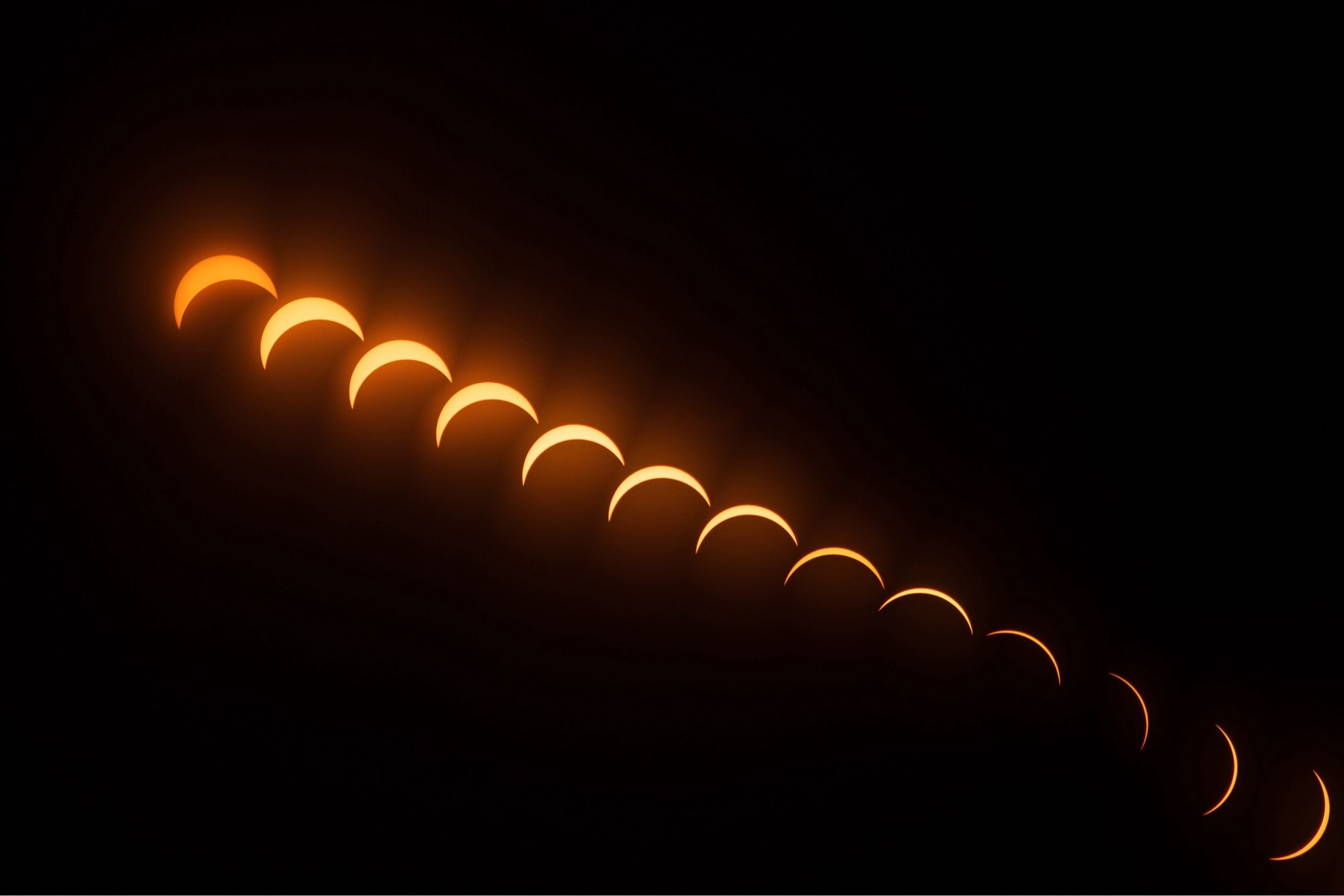 A crescent orange sun in various stages of totality moving left to right during a partial solar eclipse.