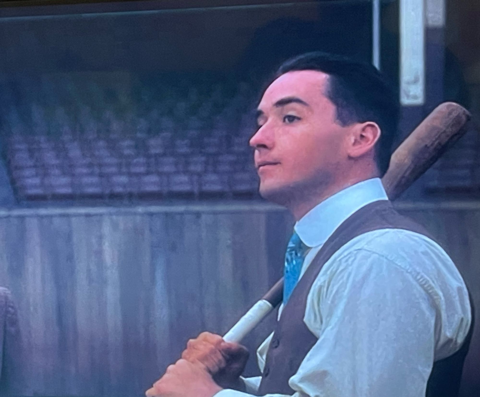 Young John Cusack as Bucky Dent, dressed in a white shirt with brown waistcoat and a blue tie, hair slicked back, a taped up baseball bat over his shoulder.