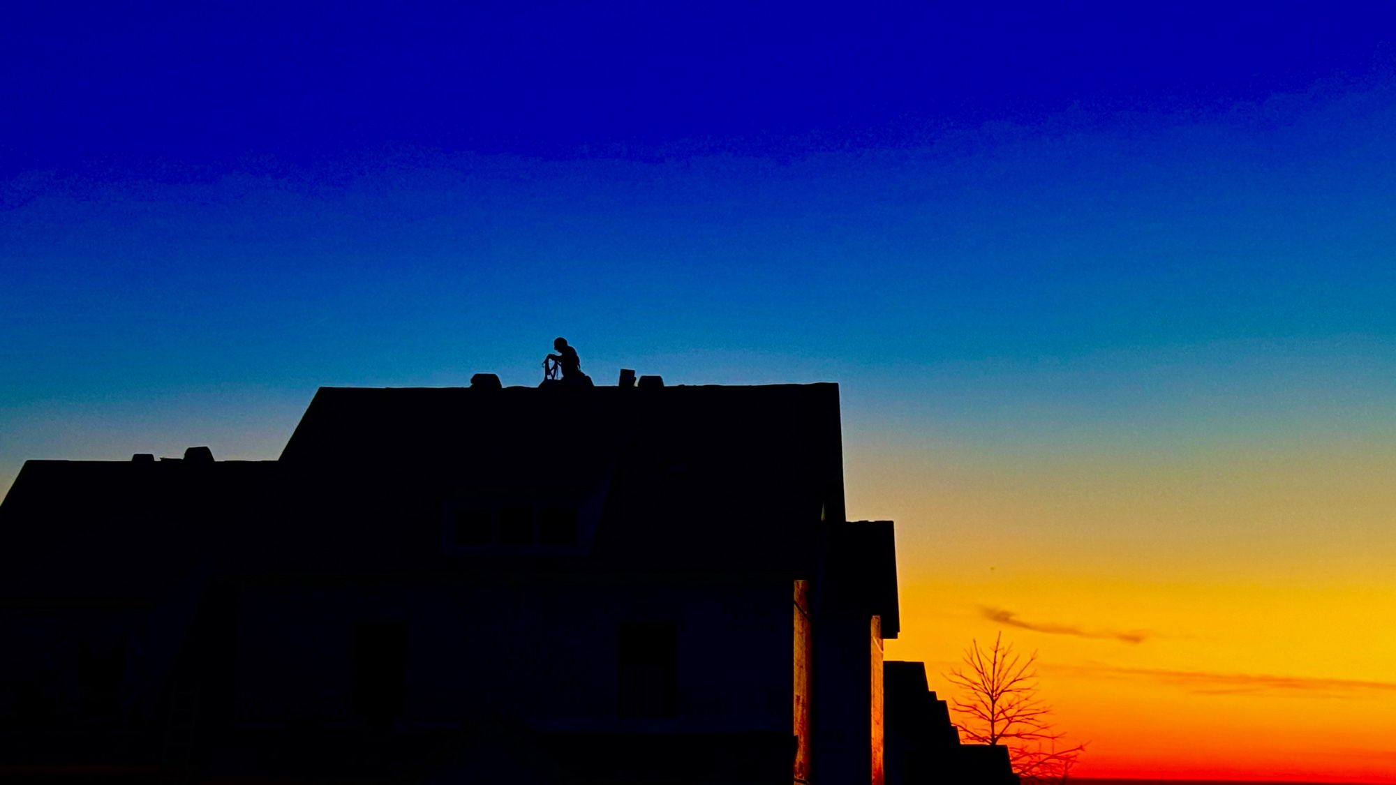 A worker on the roof of a house under construction at sunrise