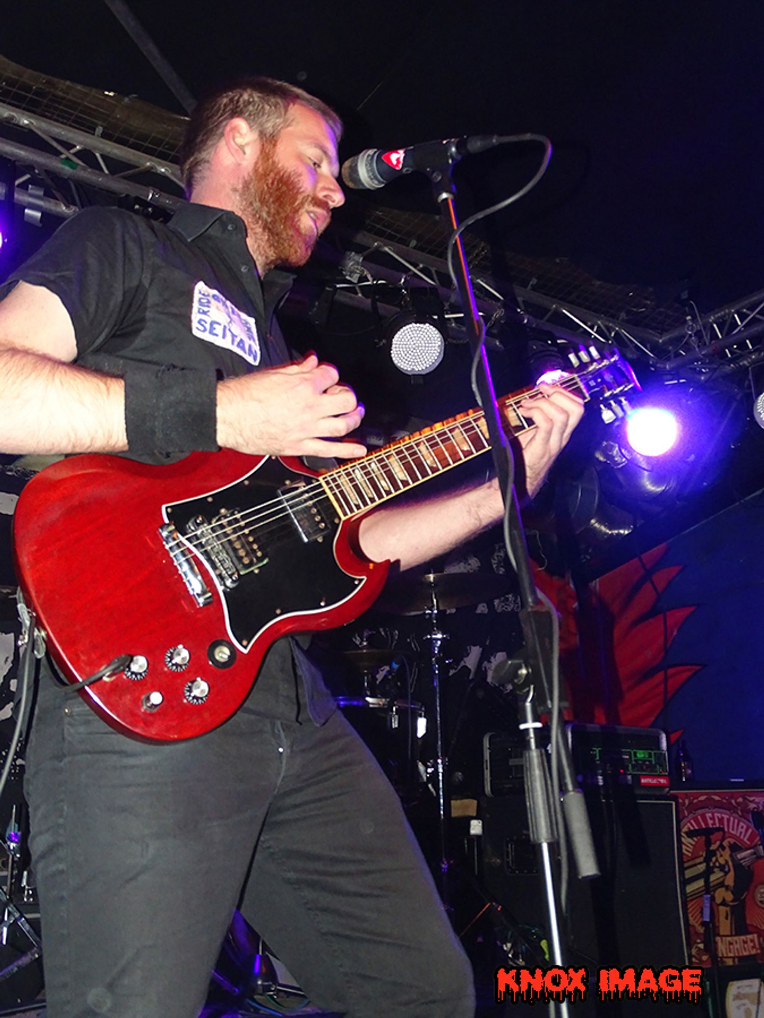 punk gittarist mit roter gitarre vor einen mikro er hat einen bart