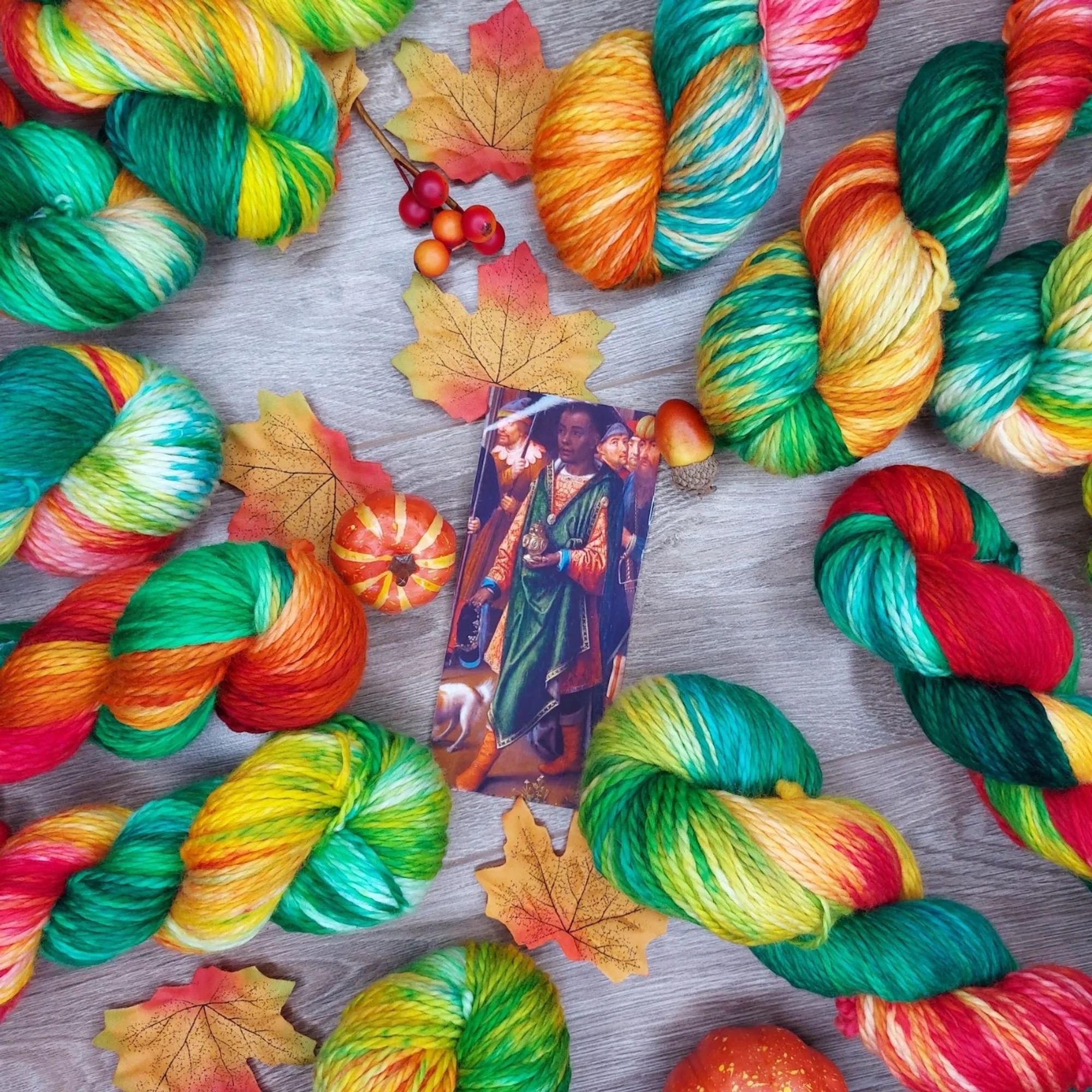 Red, yellow, and green yarn, adorned with Autumn leaves and a miniature pumpkin. A photo of a magus dressed in the same colors is also in the shot.