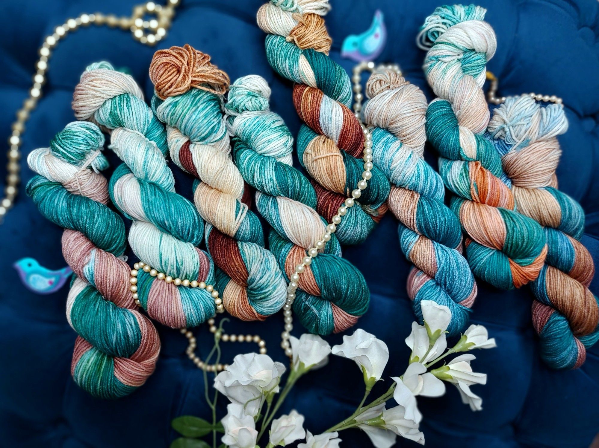 Teal and brown skeins of yarn, adorned with white flowers and pearls.