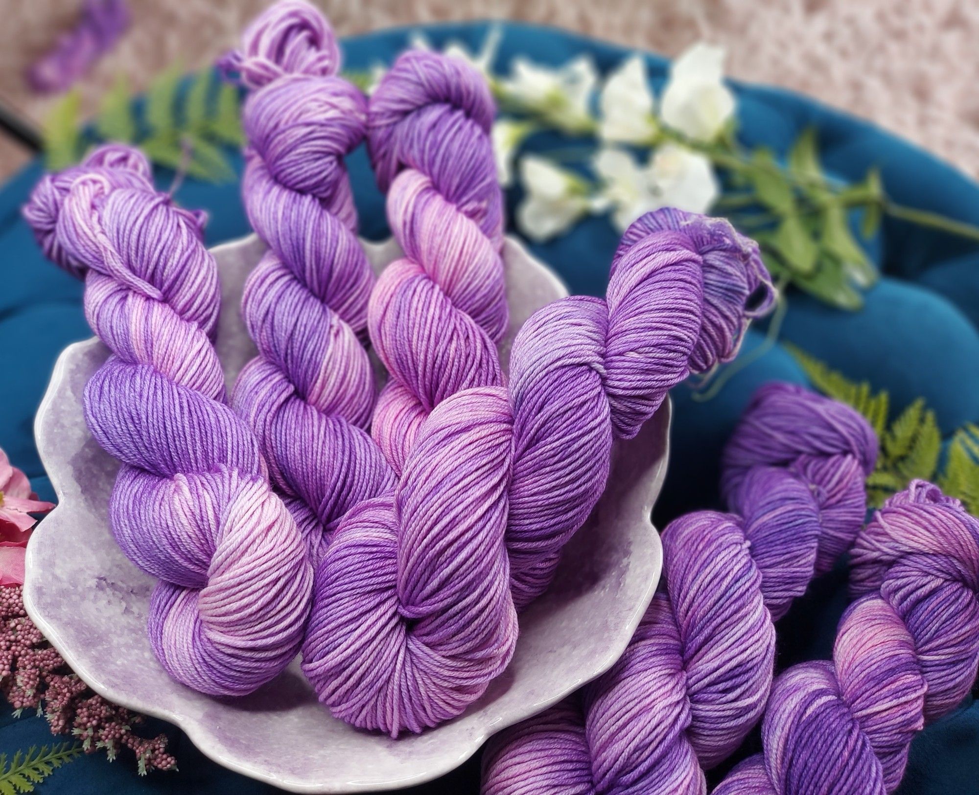 Purple and pink yarn in a bowl, adorned with pink and white flowers.