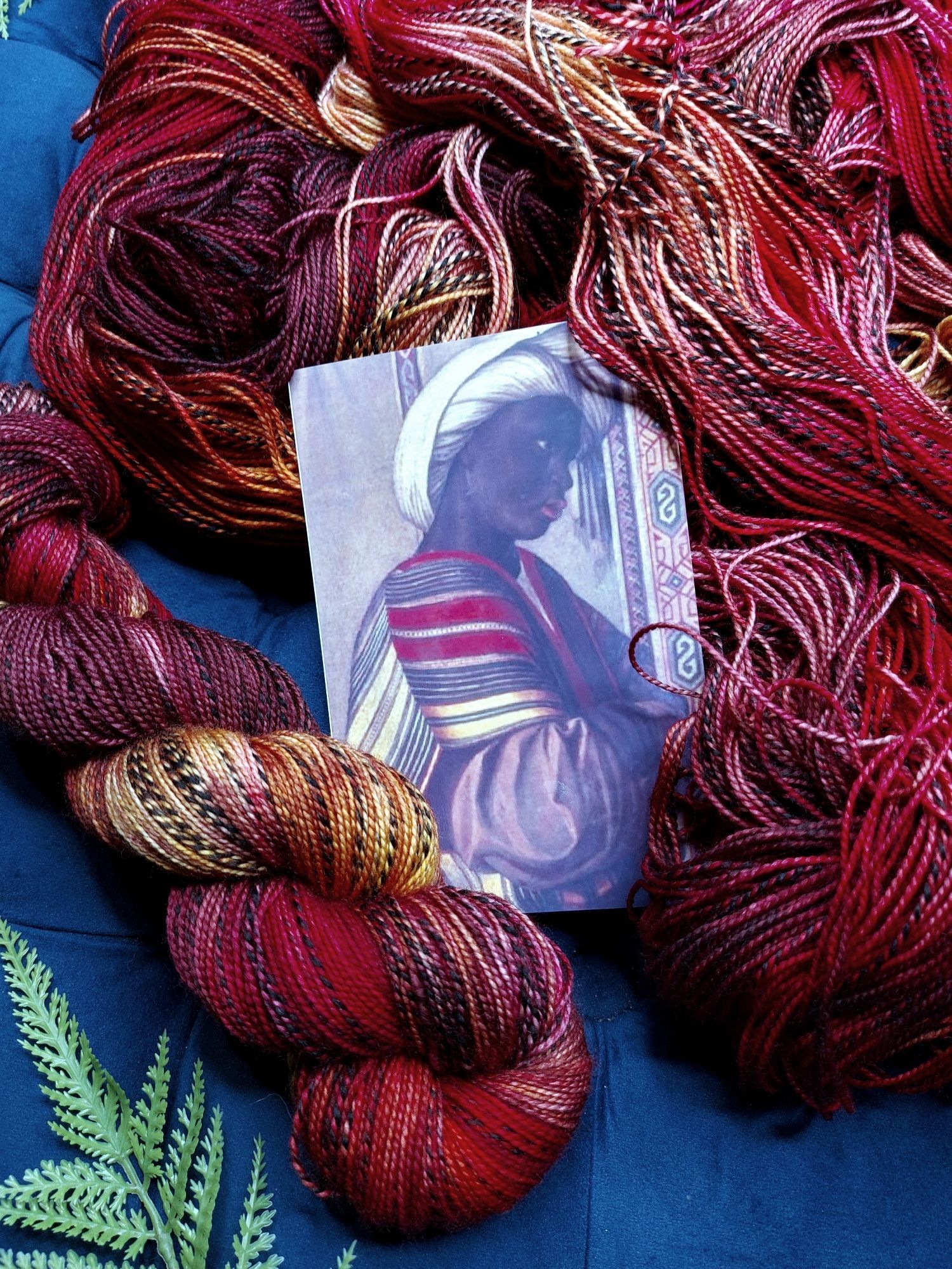 Red, gold, and black zebra pattern yarn, adorned with fern leaves. A photo of a Black servant dressed in the same colors is in the shot.