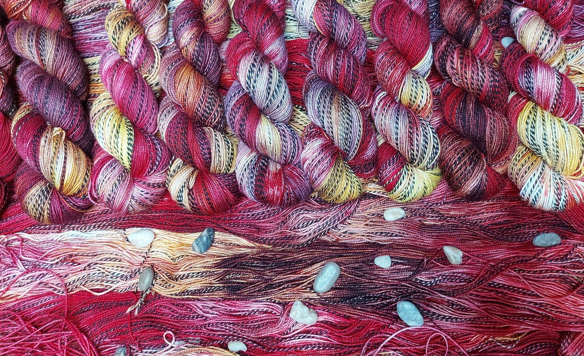 Lined up skeins of red, gold, and black zebra pattern yarn, adorned with decorative stones.