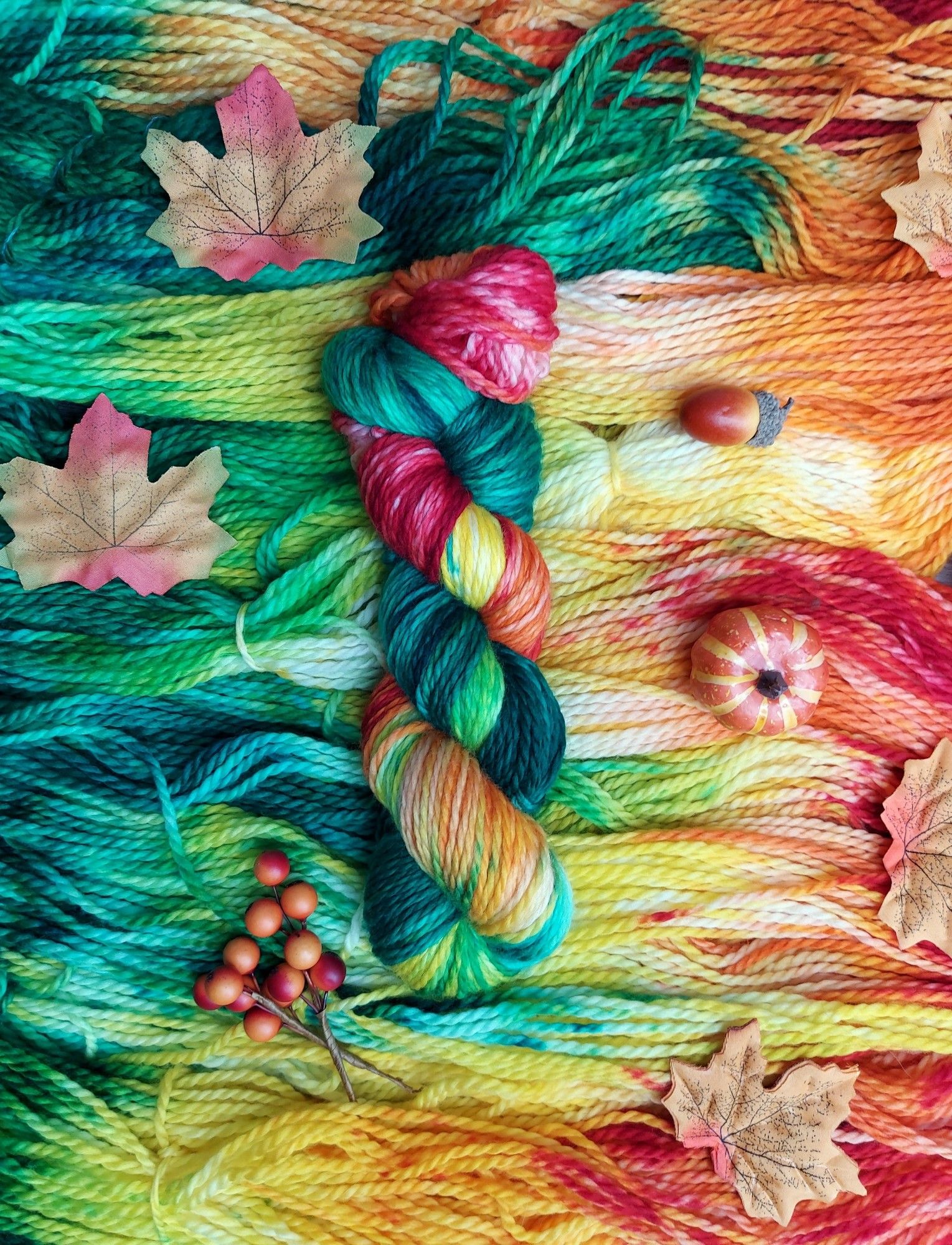 Single skein of yarn on a bed of yarn with leaves, berries and acorns around it.