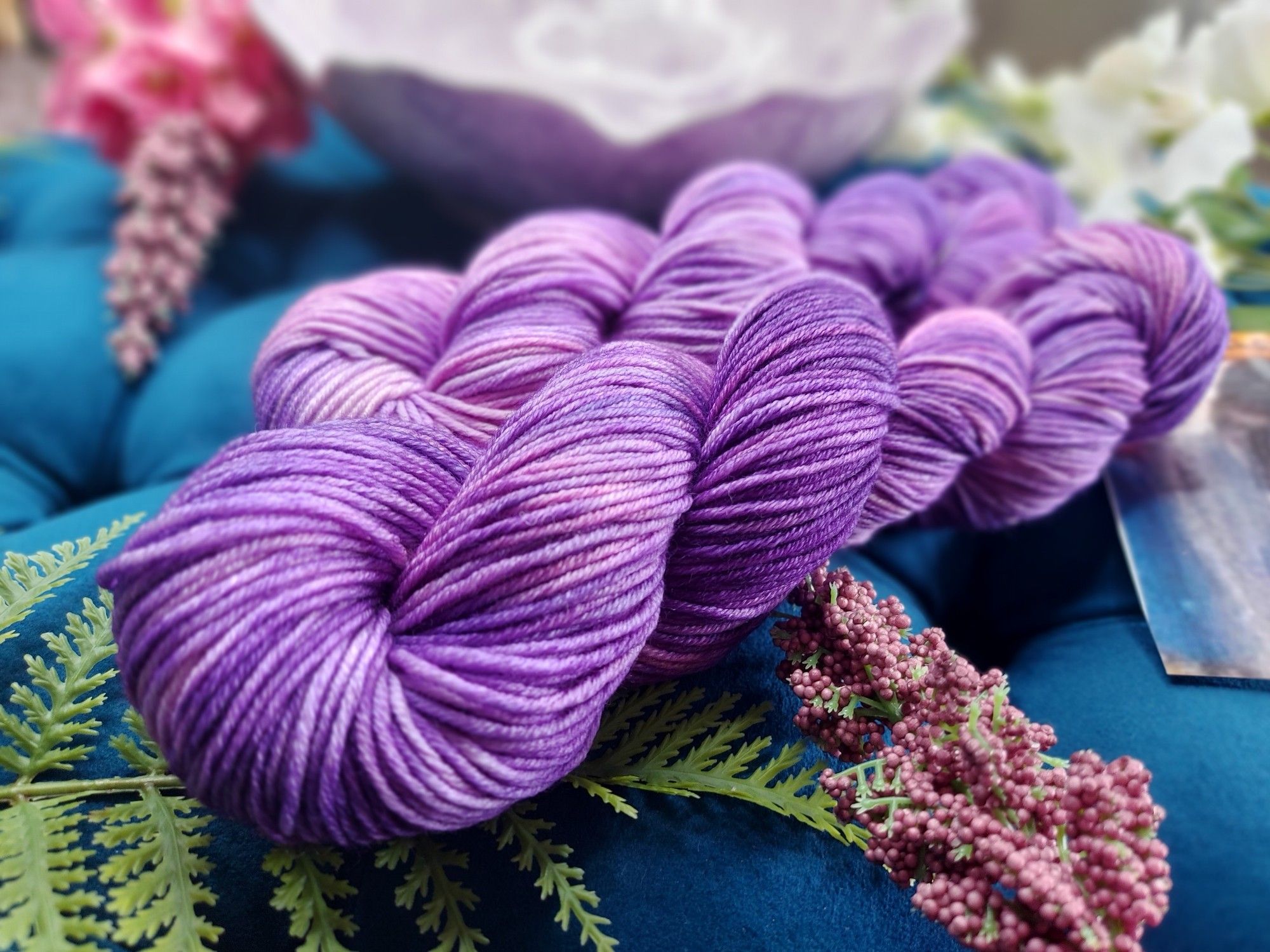 Purple and pink yarn, adorned with pink and white flowers. A decorative bowl is in the background.