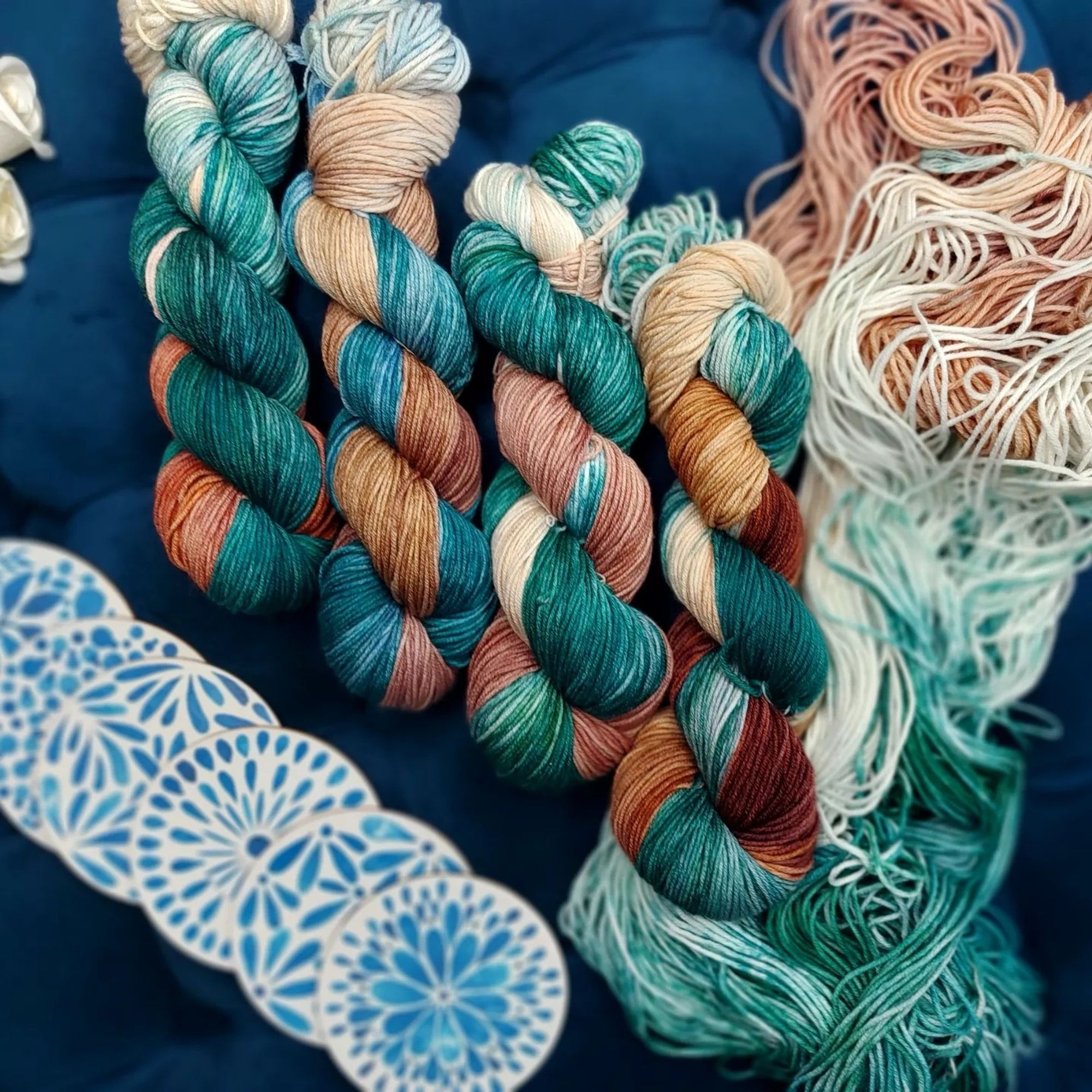 skeins of mystic magi teal with one open skein on the right. A few blue and white coasters in the bottom left