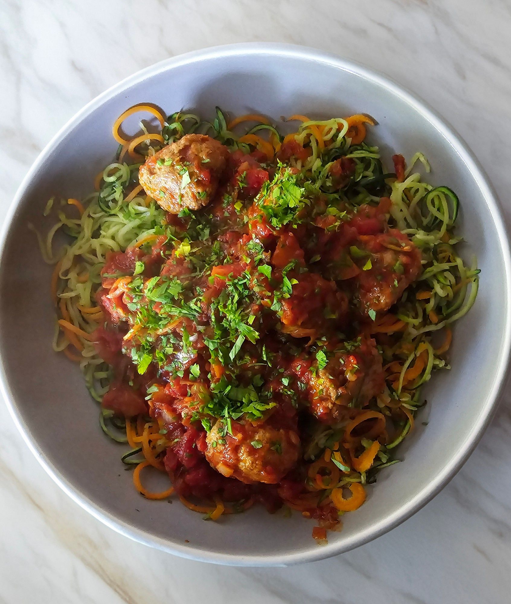 A serving bowl of turkey meatballs in a rich spicy tomato sauce with courgetti noodles.