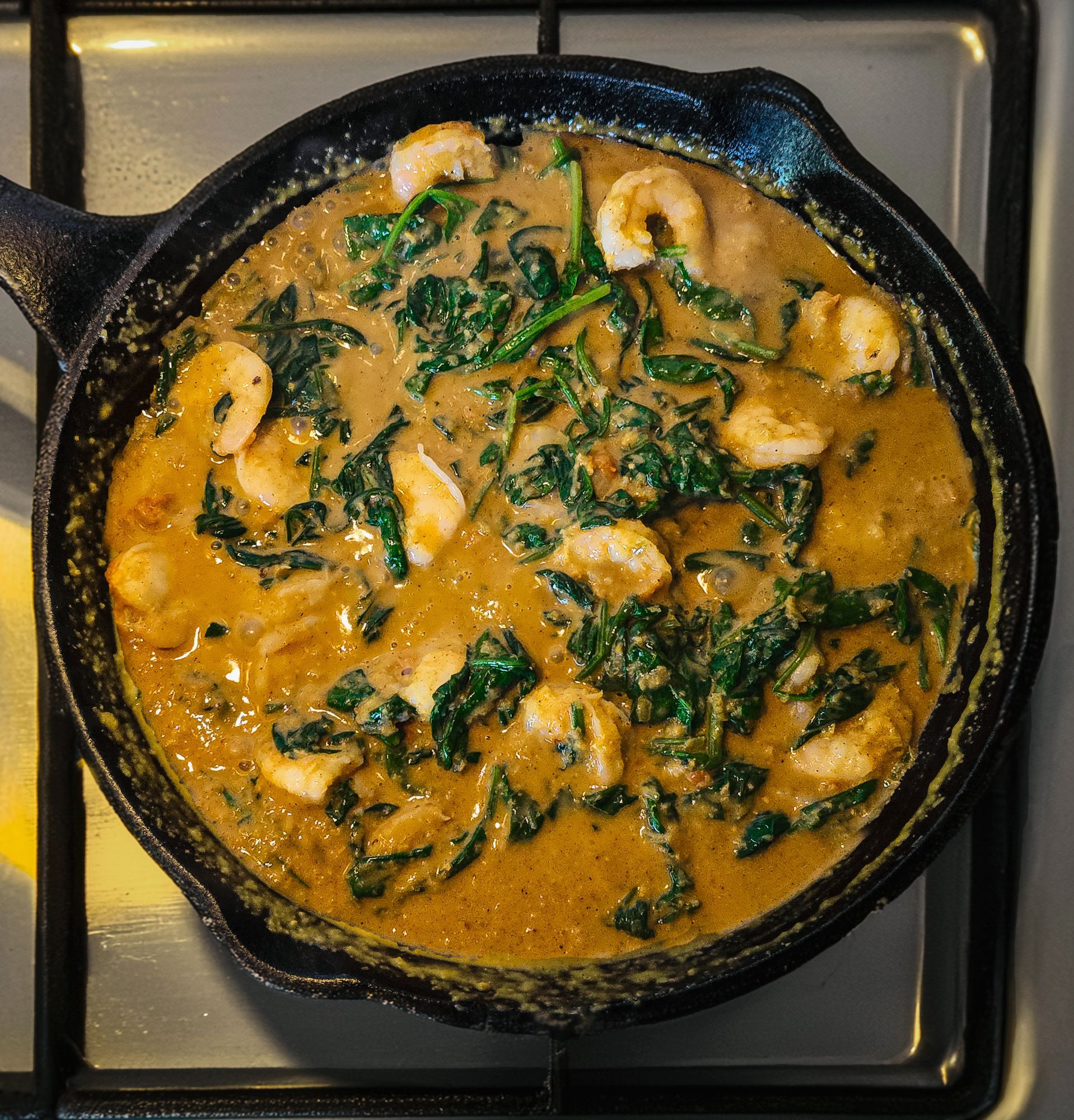 A fragrant prawn and spinach curry simmer gently in a cast iron pan on a hob.