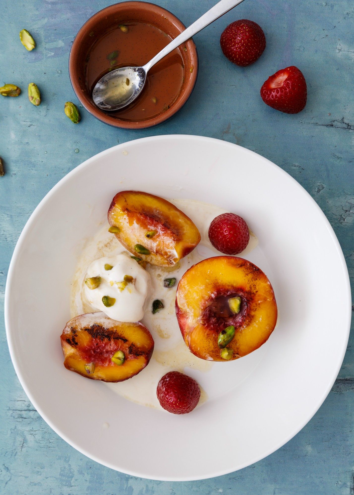 Delicious summer treat: grilled nectarines paired with creamy vanilla ice cream, honey drizzle, a pistachio garnish, and an added strawberry just for fun!