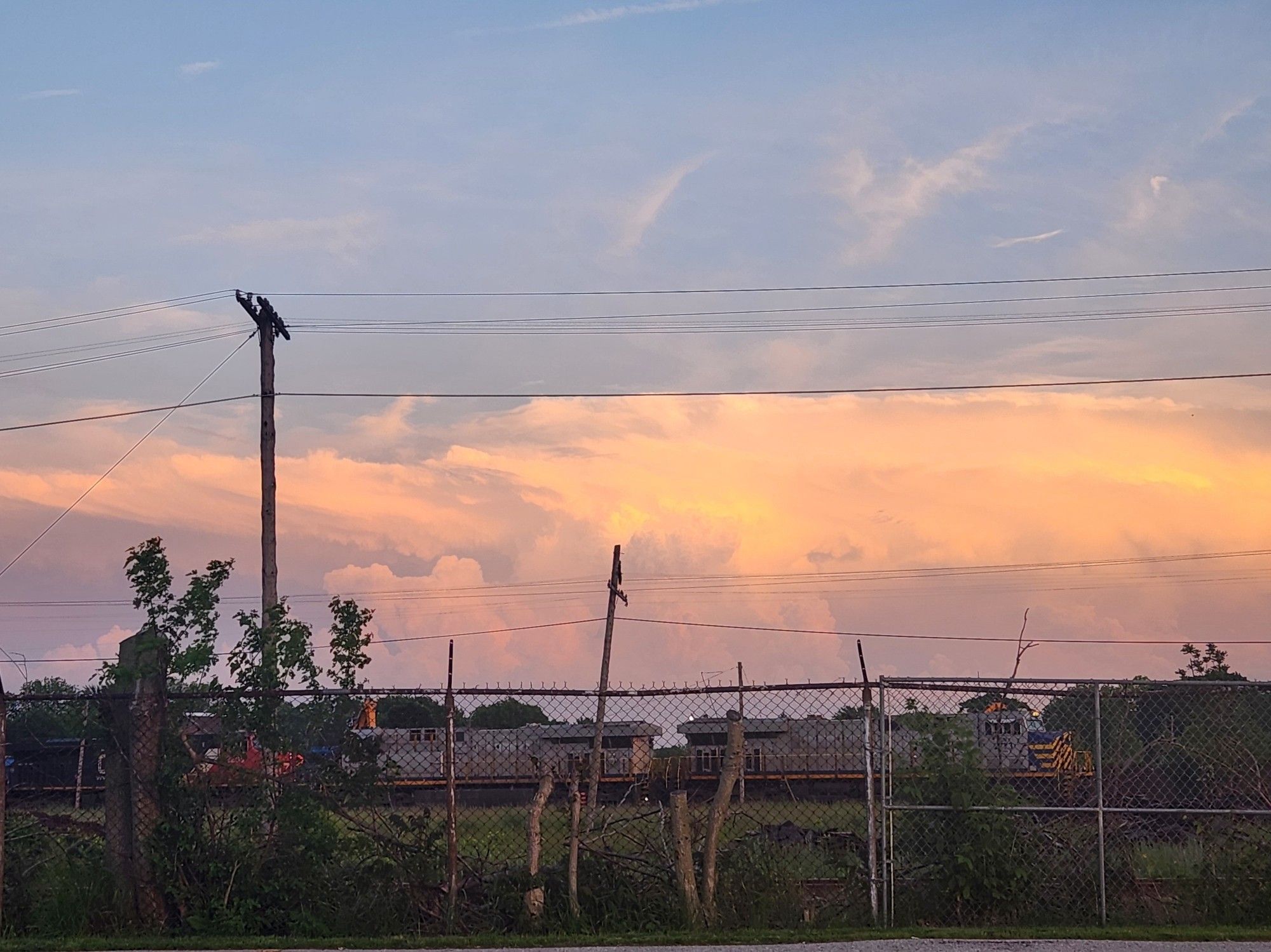 Some idling train engines behind a fence with the evening sky behind