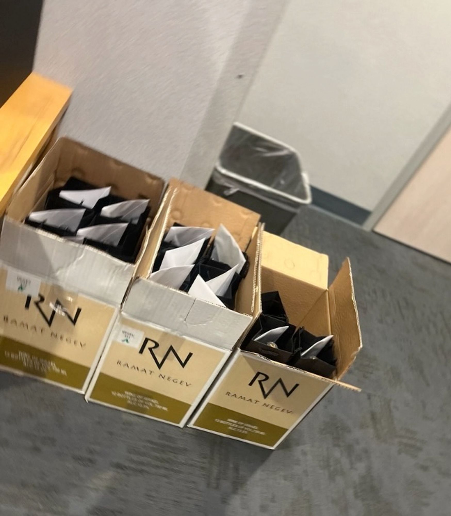 Three open cases of Ramat Negev wine on the floor of an office. Each wine bottle has a personalized letter envelope attached to it.