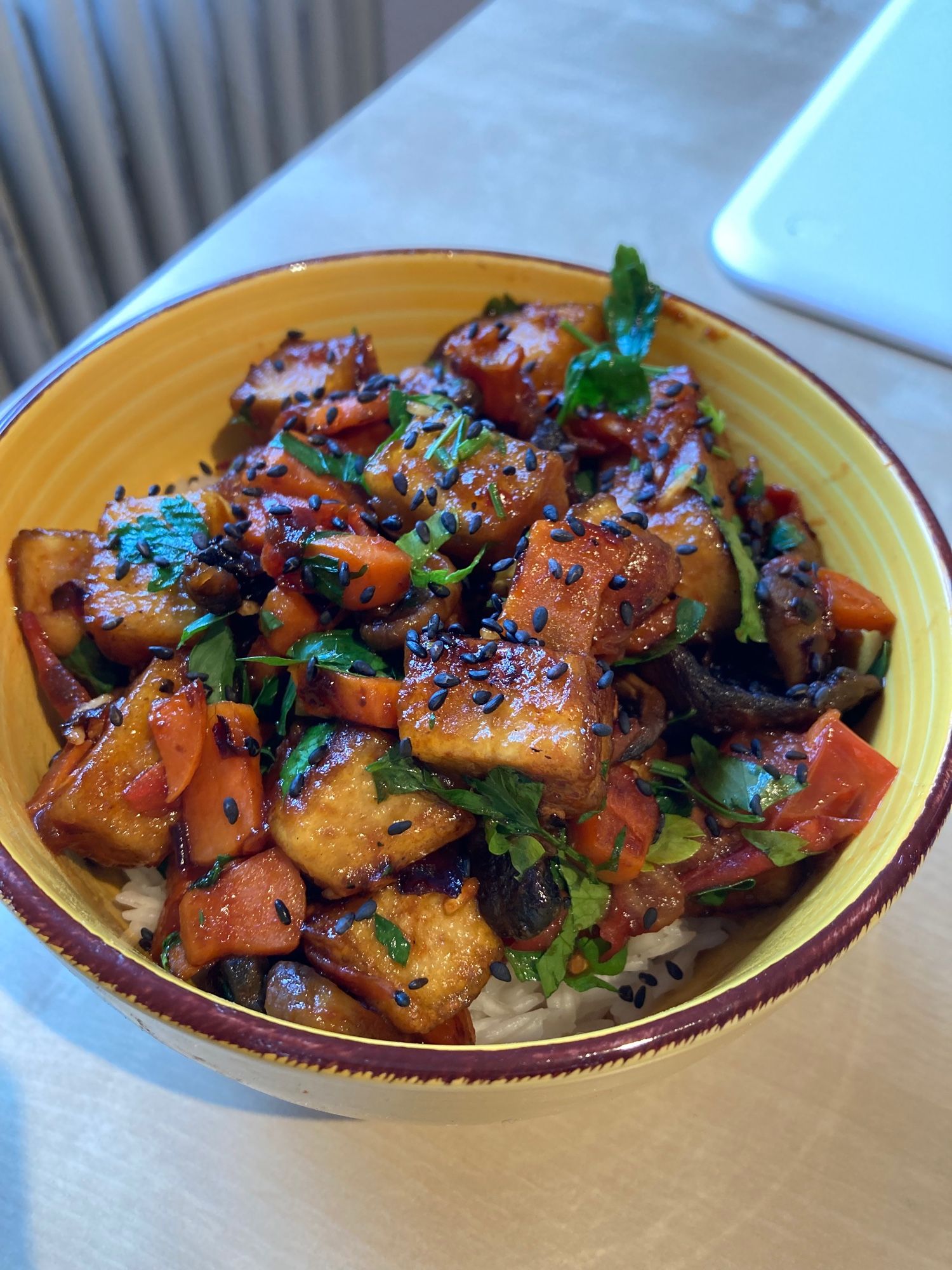 Müslischüssel mit Tofu, Karotten und Champignons. Außerdem ist gehackte Petersilie zu sehen. Darauf ist gerösteter Sesam zu sehen.