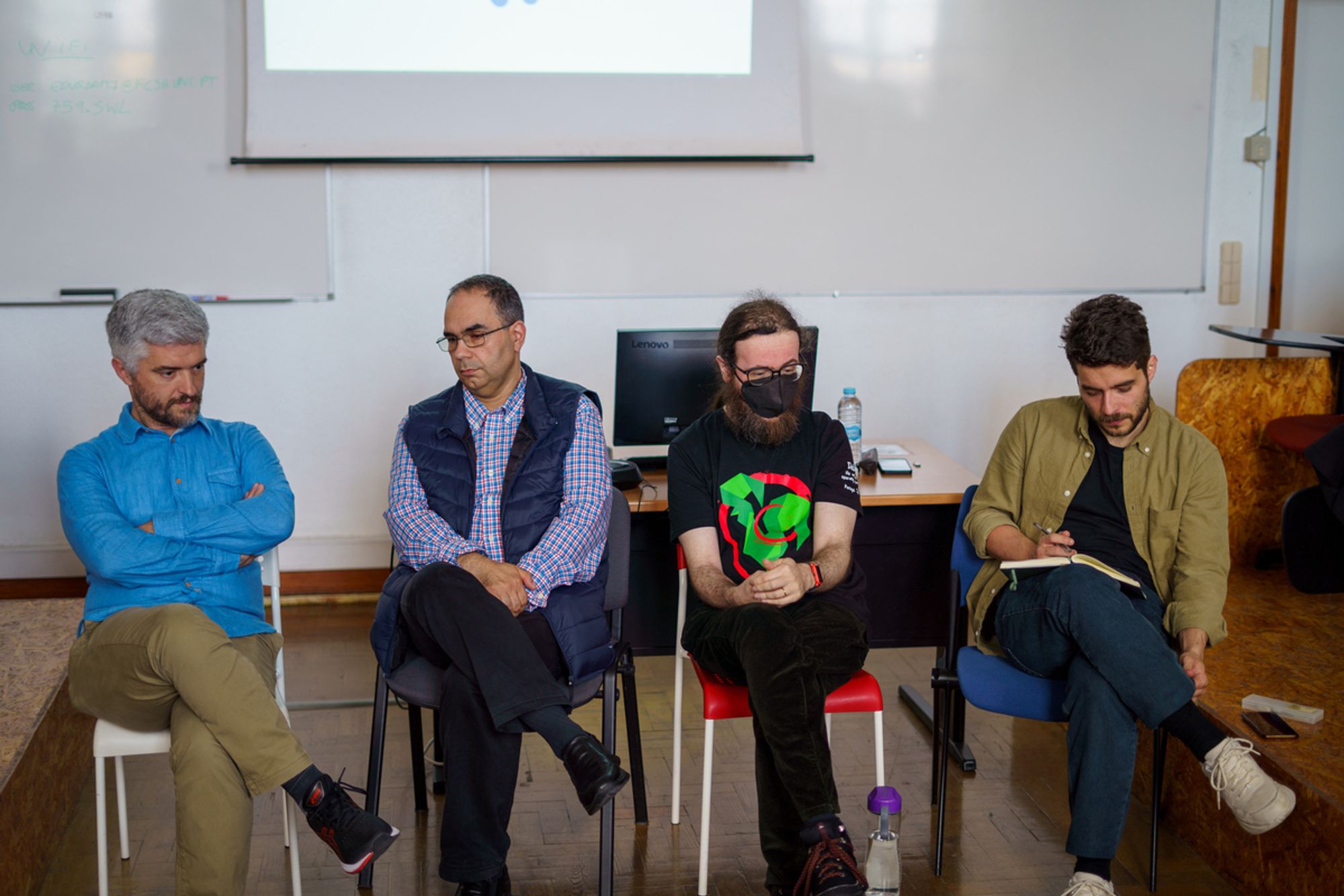 Four persons sitting in chairs in a classroom to start a conference about the importance of open standards, in 2023.