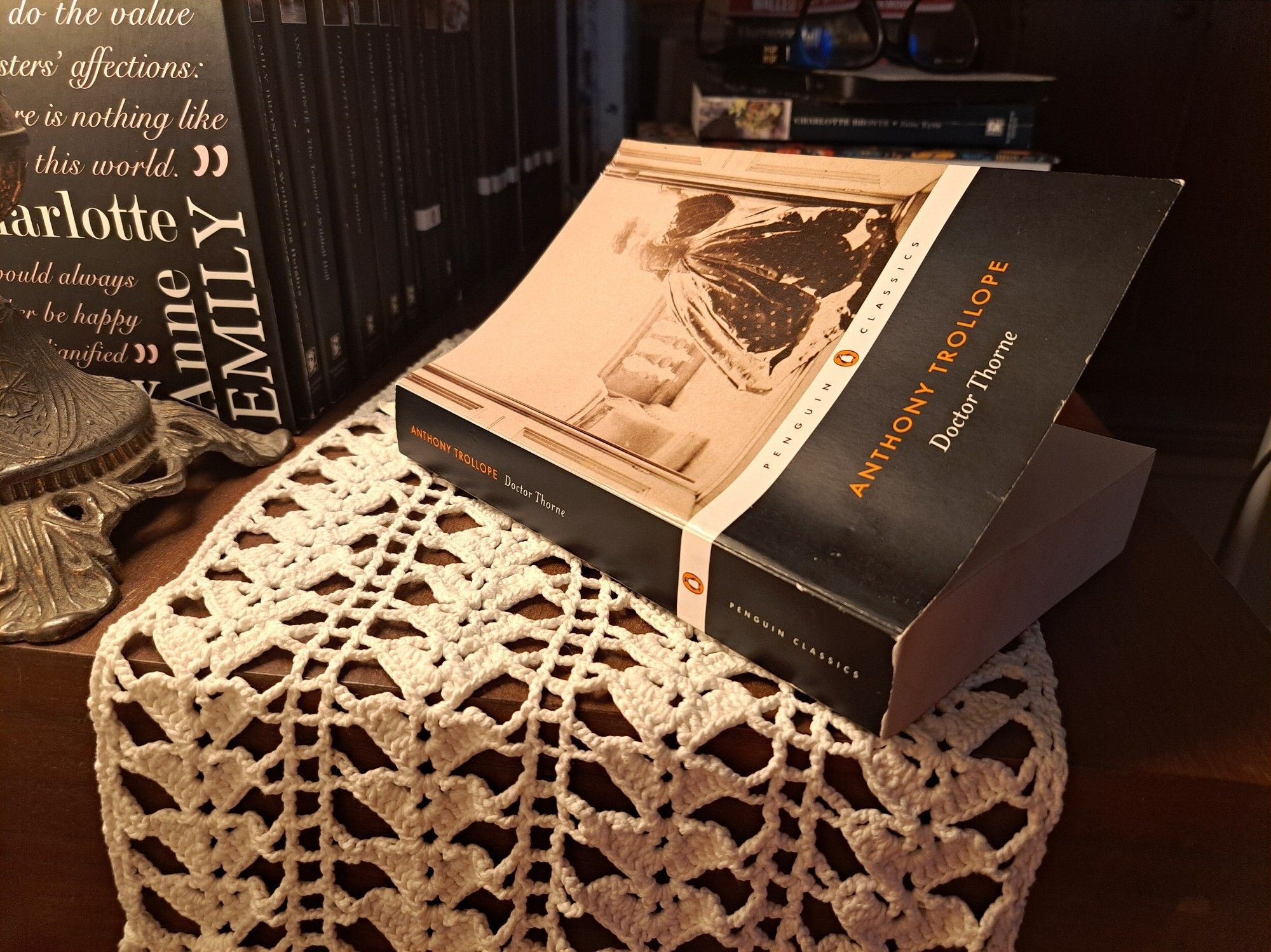 The book (black and white) over a white crochet cloth in front of other books and a parte of a lamp on the aide