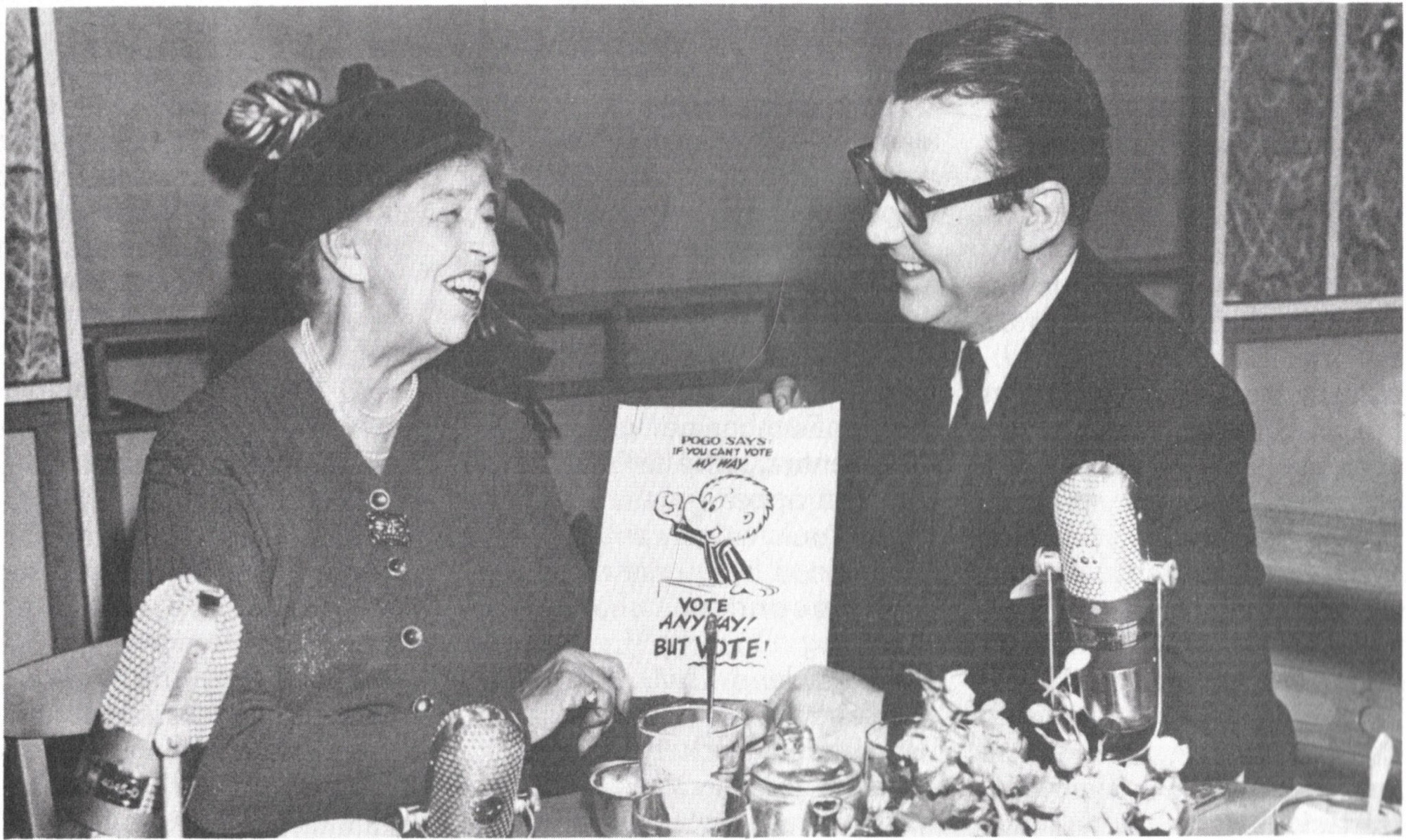 Roosevelt and Kelly sitting at a table together, holding a cartoon of Pogo saying “If you can’t vote my way, vote anyway! But vote!”