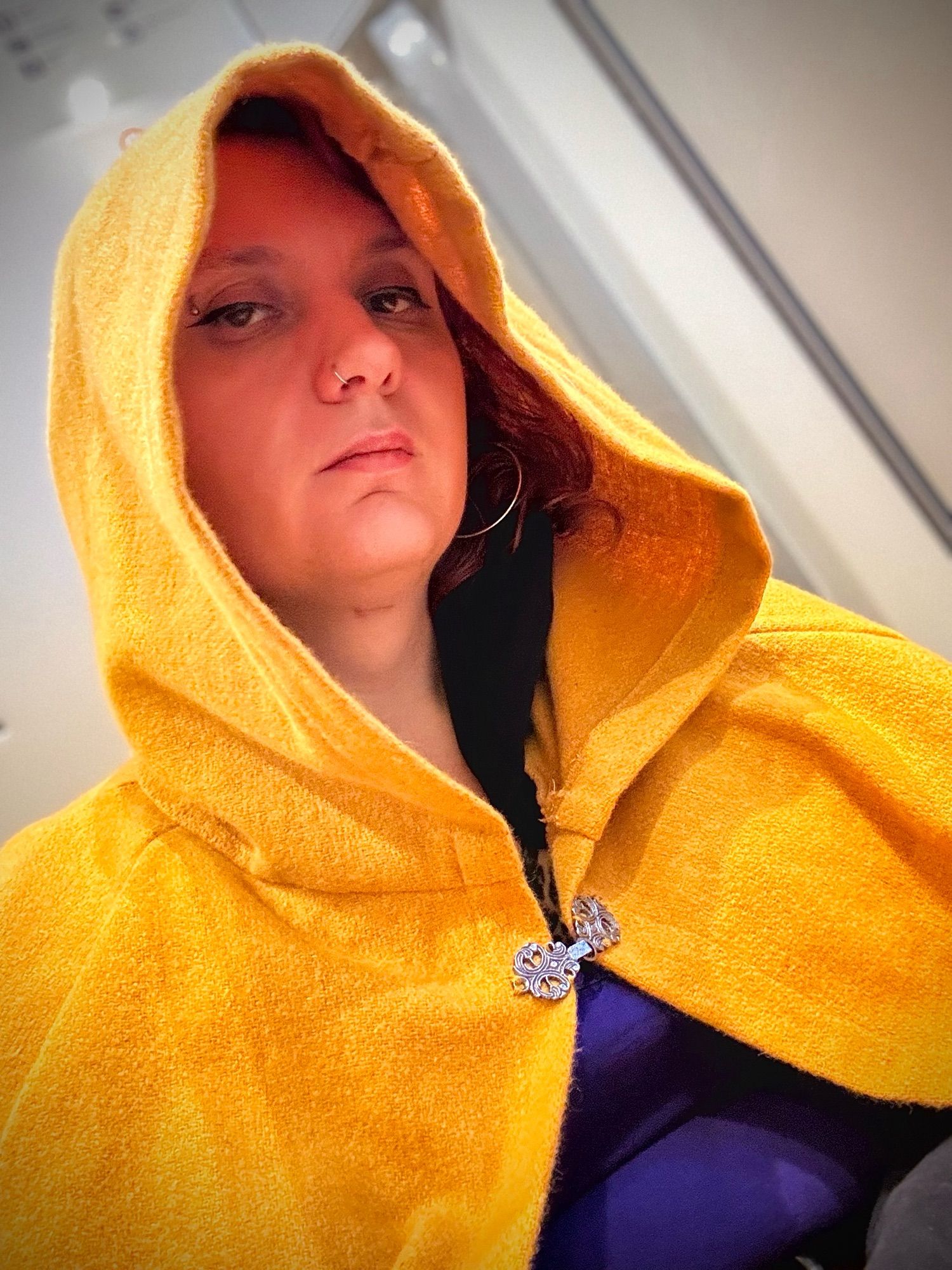 Andrea looking mysteriously at the camera out from under the hood of a yellow wool cloak