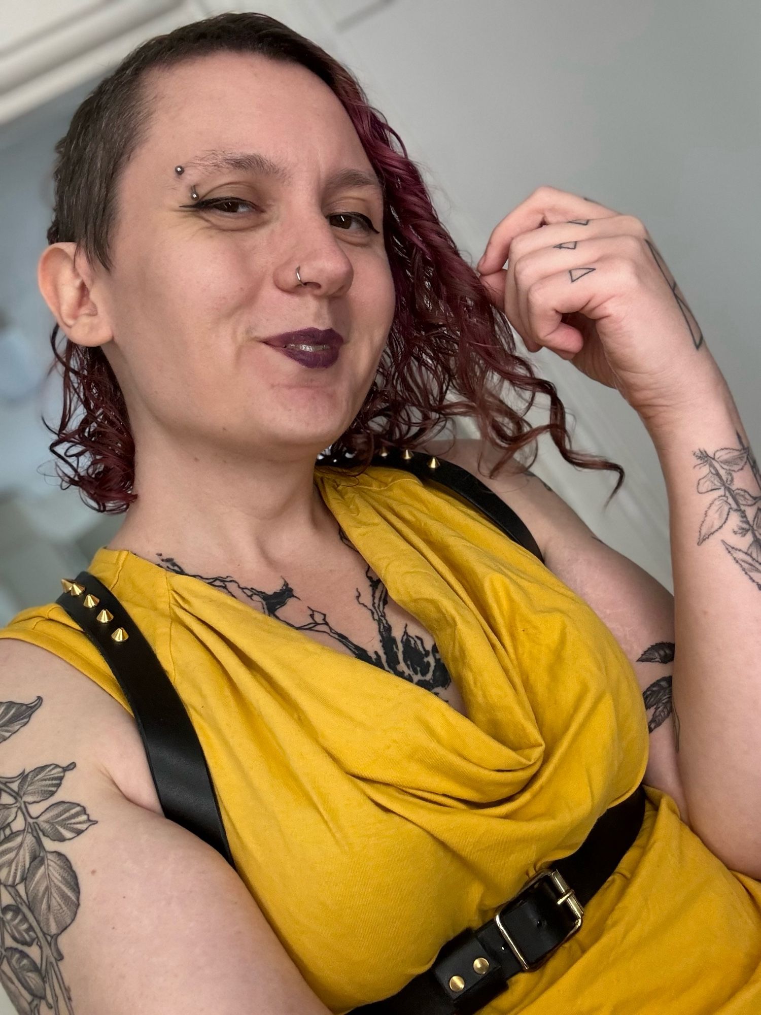 Andrea smiling at the camera, wearing a bright yellow tanktop and a black leather harness with brass hardware