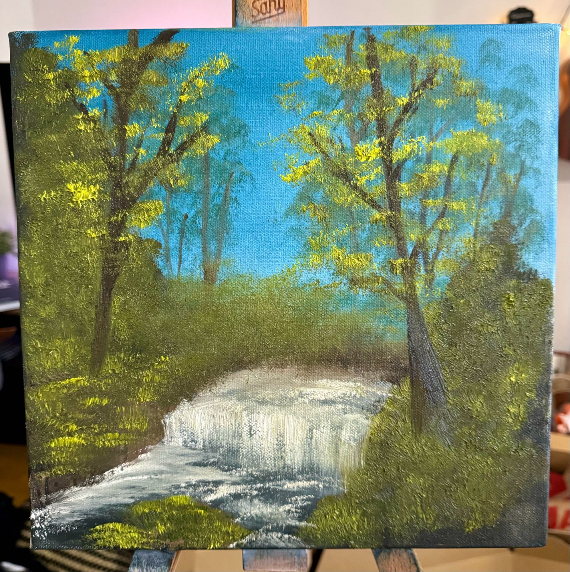 An oil painting of a creek in a blurry forest in the style of Bob Ross (but if Bob had never used oil paint before)