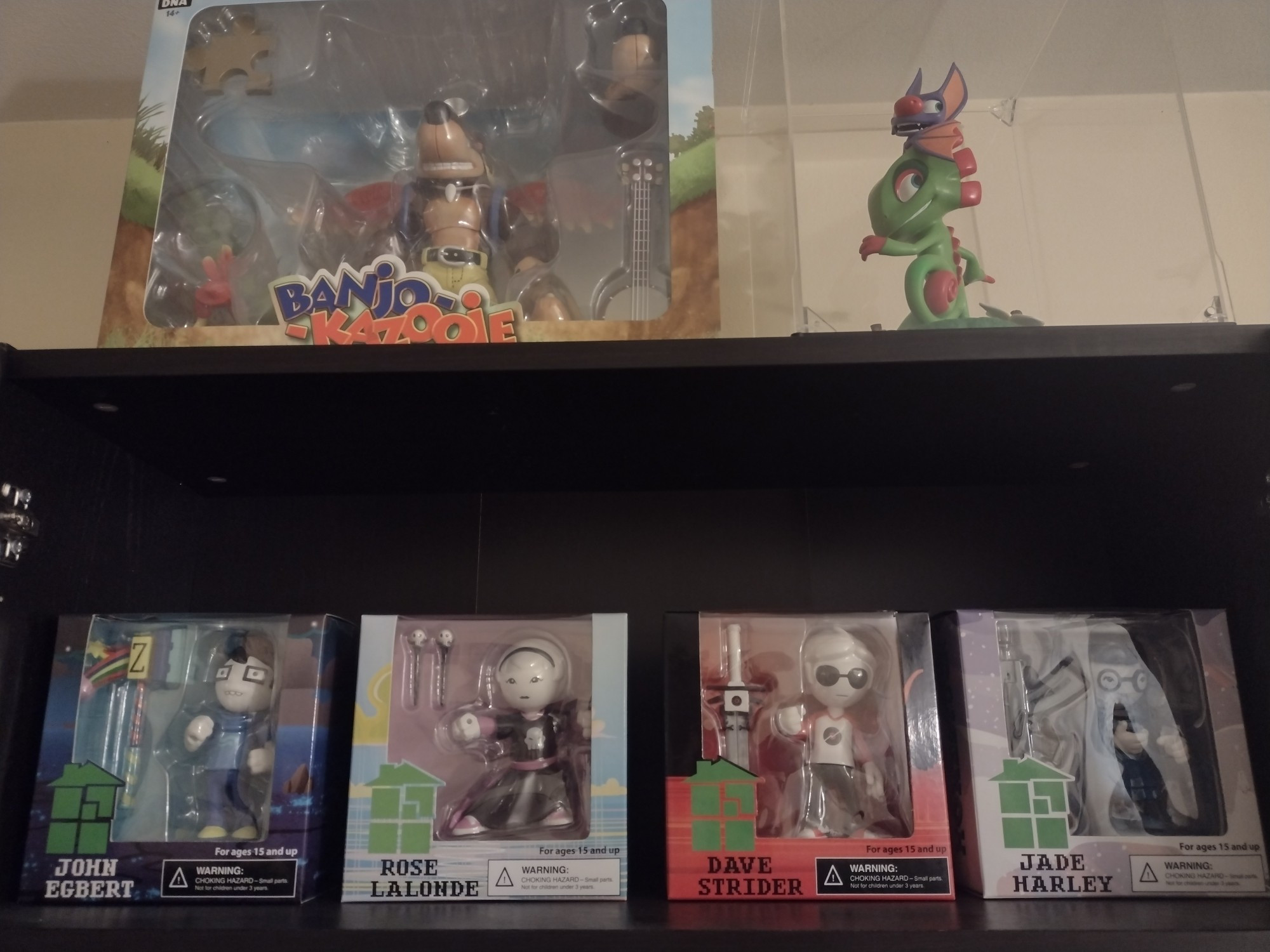 A photo of four Homestuck vinyl figures on a bookshelf, with two Banjo-Kazooie and Yooka-Laylee figures watching over them on the shelf above.