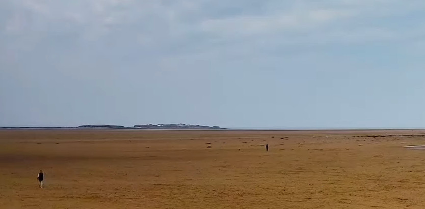 West Kirby beach with Hilbre Island on the horizon, a couple of people walking on the beach.