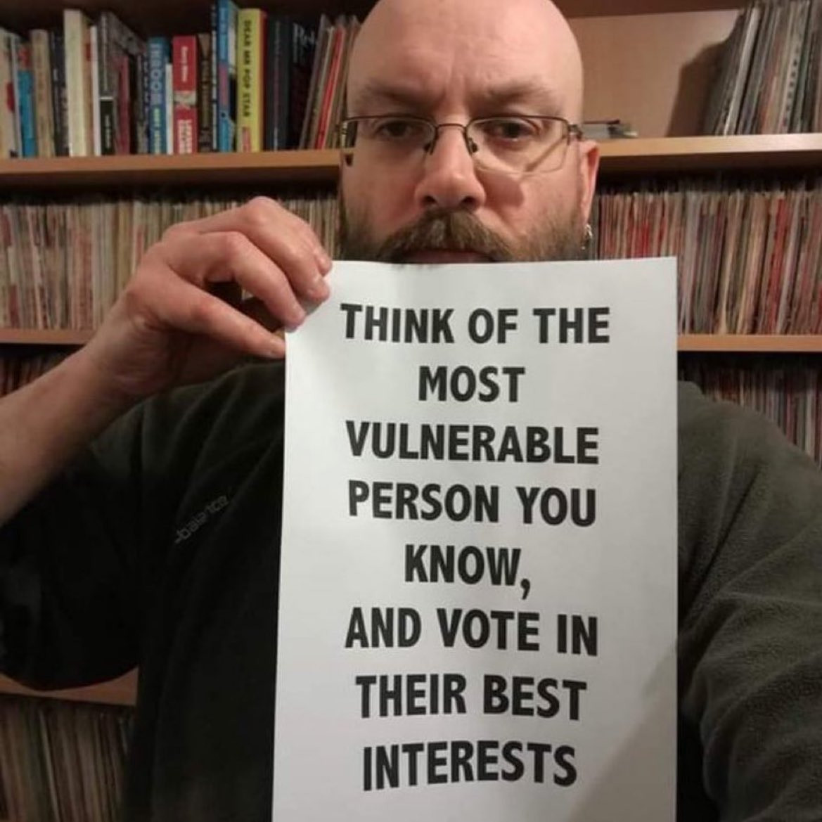 Person holding up a sign that reads, "Think of the most vulnerable person you know, and vote in their best interests".