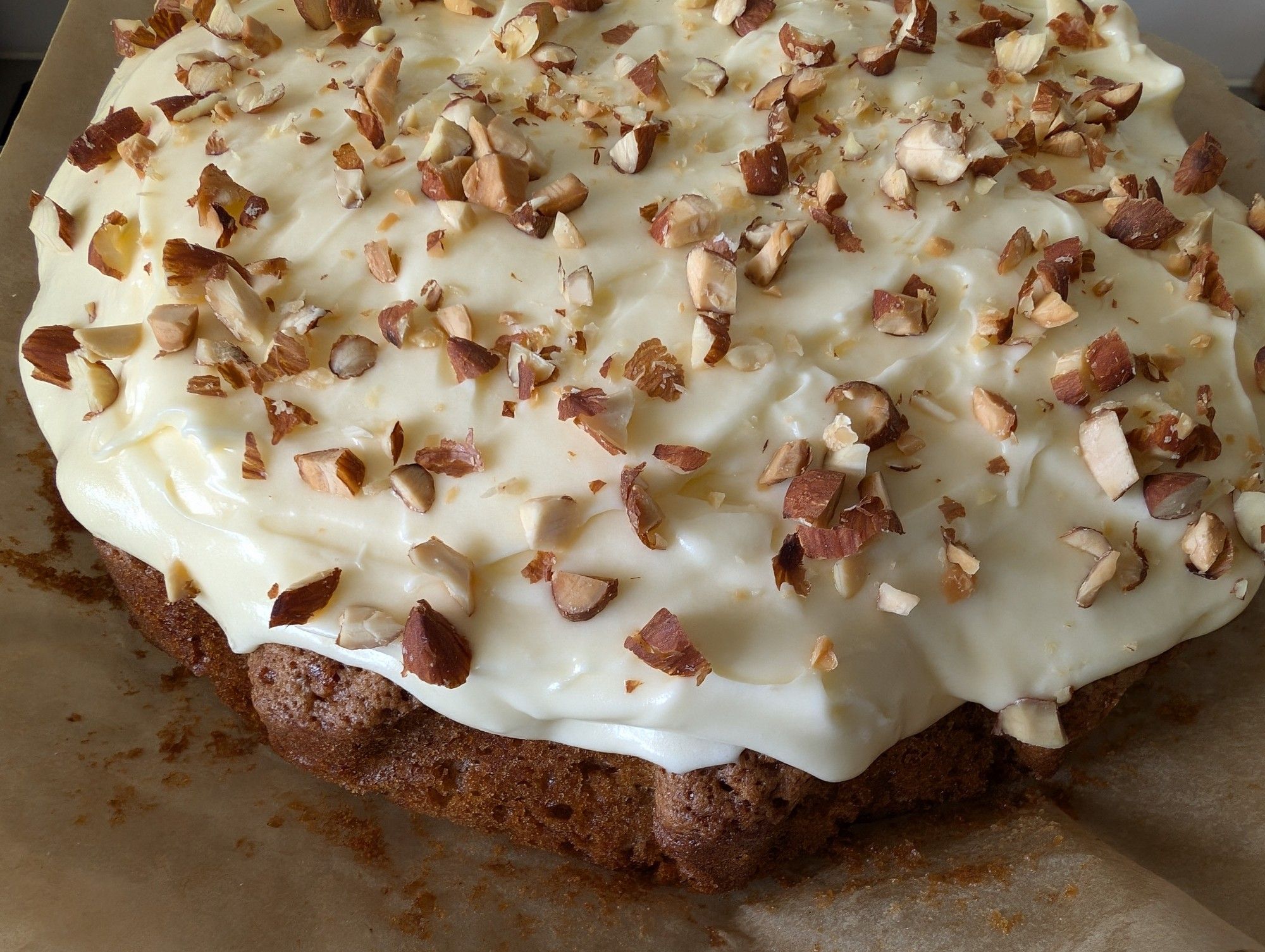 A homemade carrot cake with cream cheese frosting and chopped roasted almonds sprinkled on top.