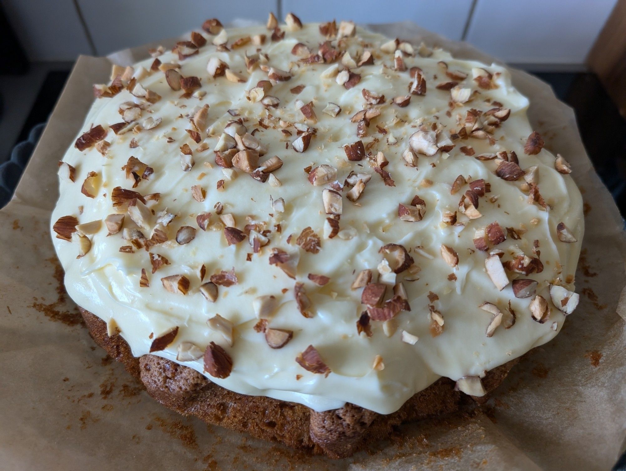 A homemade carrot cake with cream cheese frosting and chopped roasted almonds sprinkled on top.