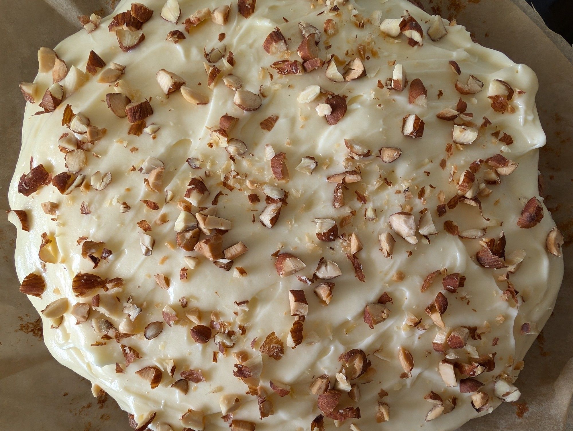 A homemade carrot cake with cream cheese frosting and chopped roasted almonds sprinkled on top.