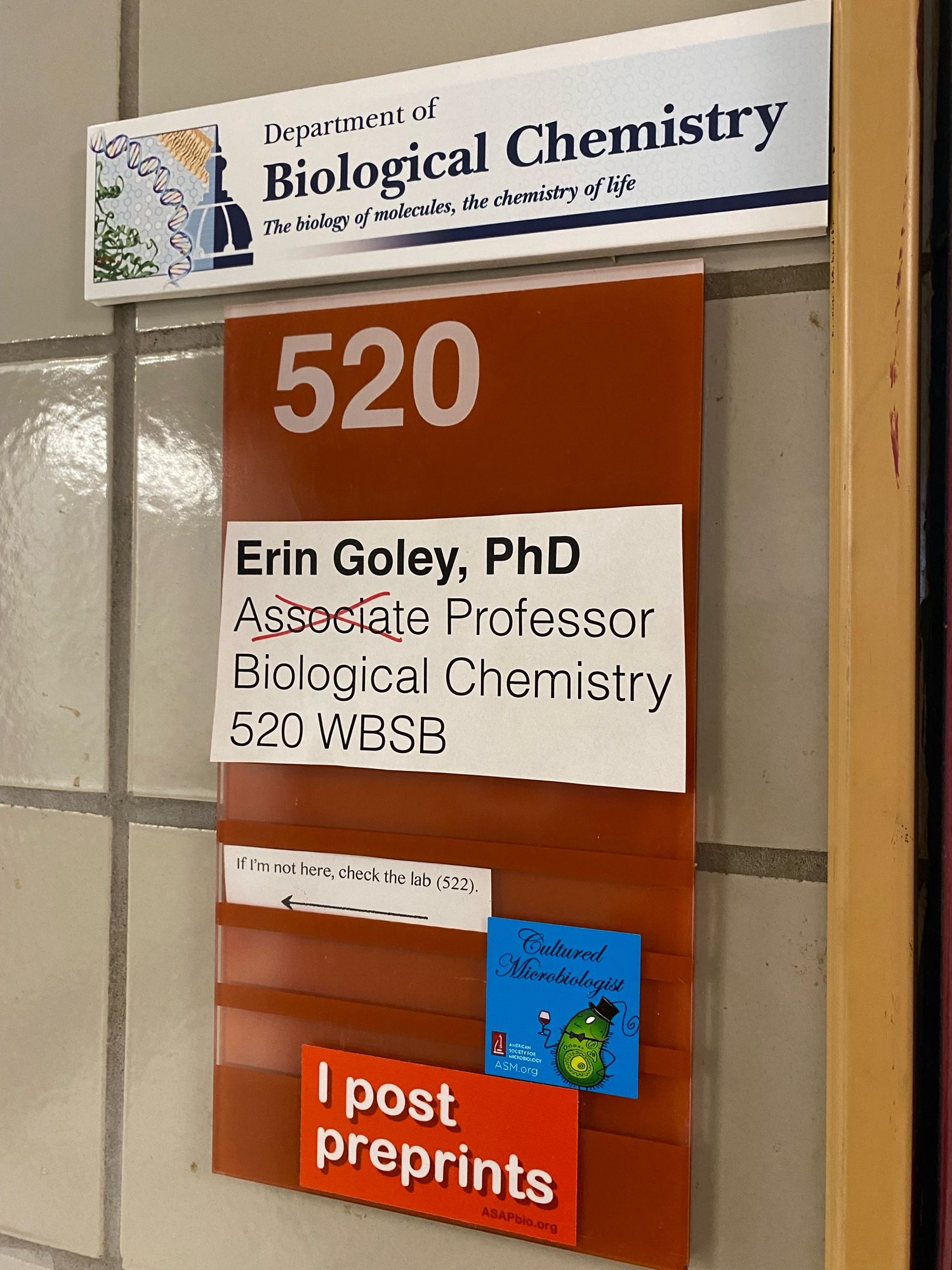 Door sign reading “Erin Goley, PhD, Associate Professor, Biological Chemistry, 520 WBSB”, with a red X through “Associate”.