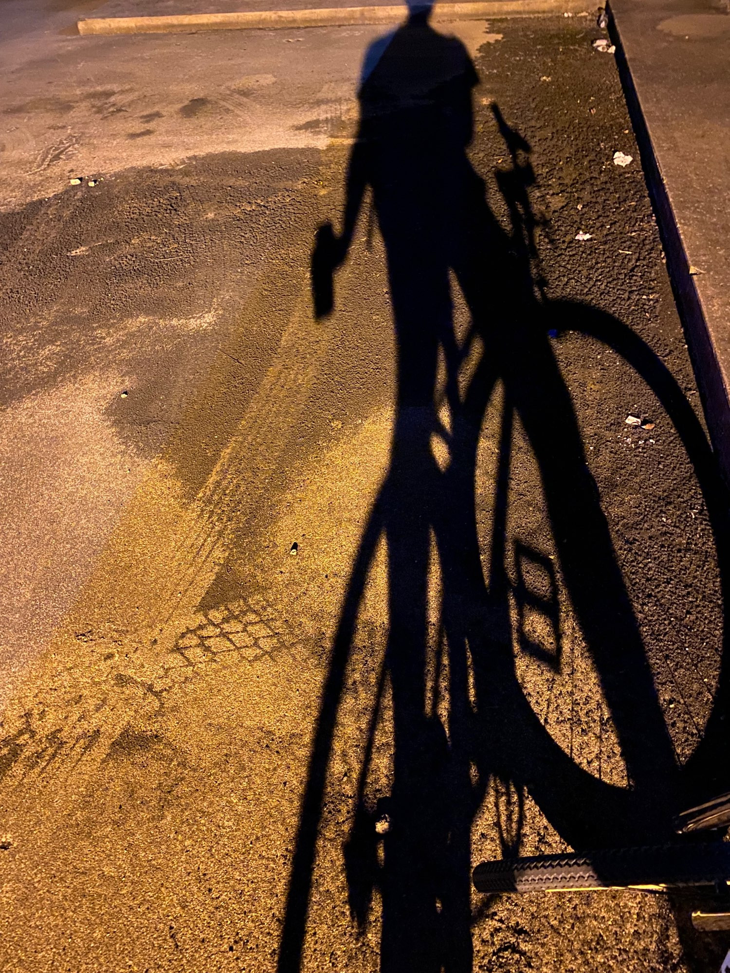 Shadow of a man on bicycle drinking a tall IPA at an above ground parking garage 