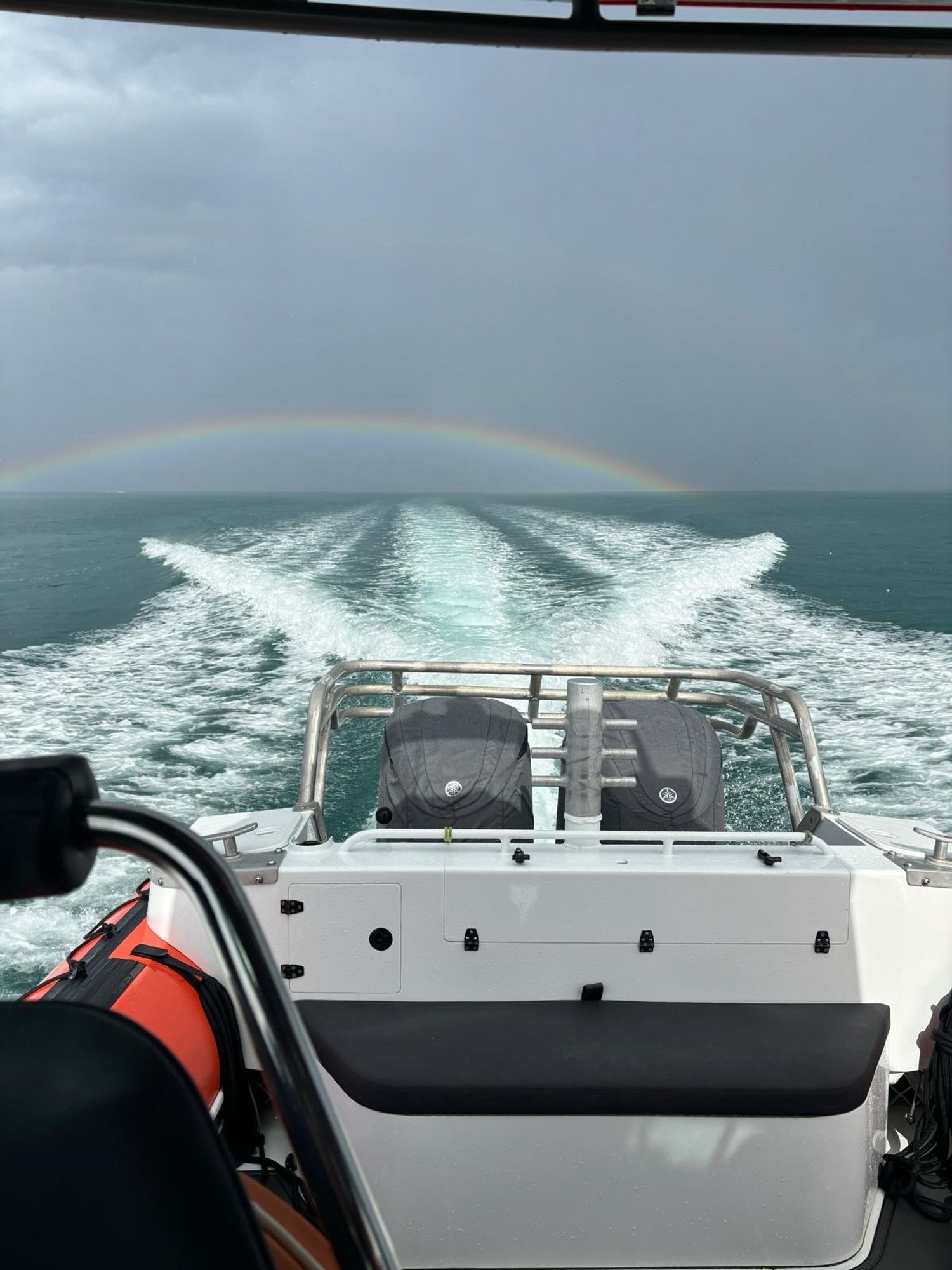 View from the stern of Hibiscus Rescue 1 showing the twin outboards, boat wake and a rainbow in the approaching thunderstorm