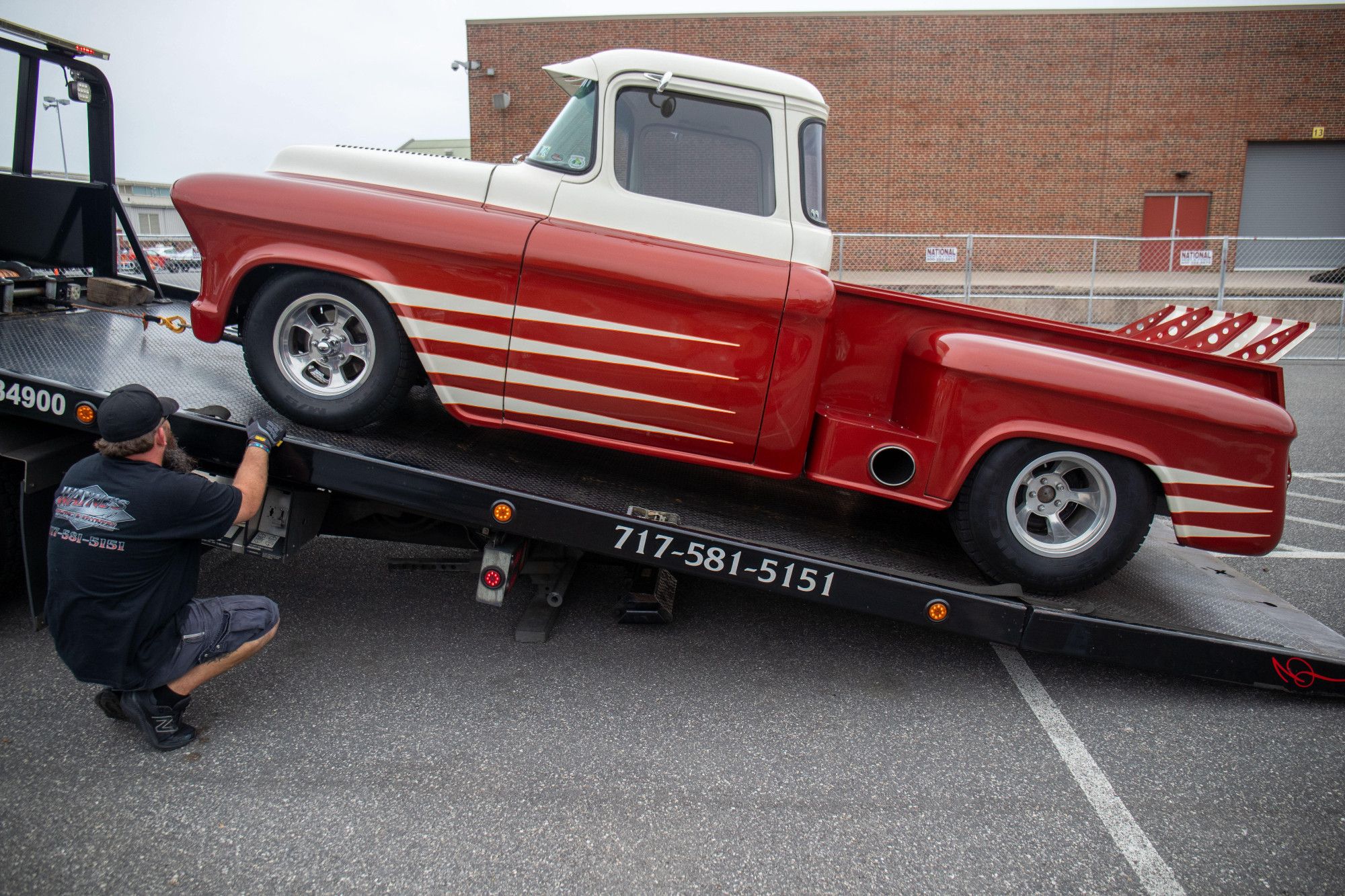 A red and white 955 Chevy Apache truck being unloaded from a towing truck.