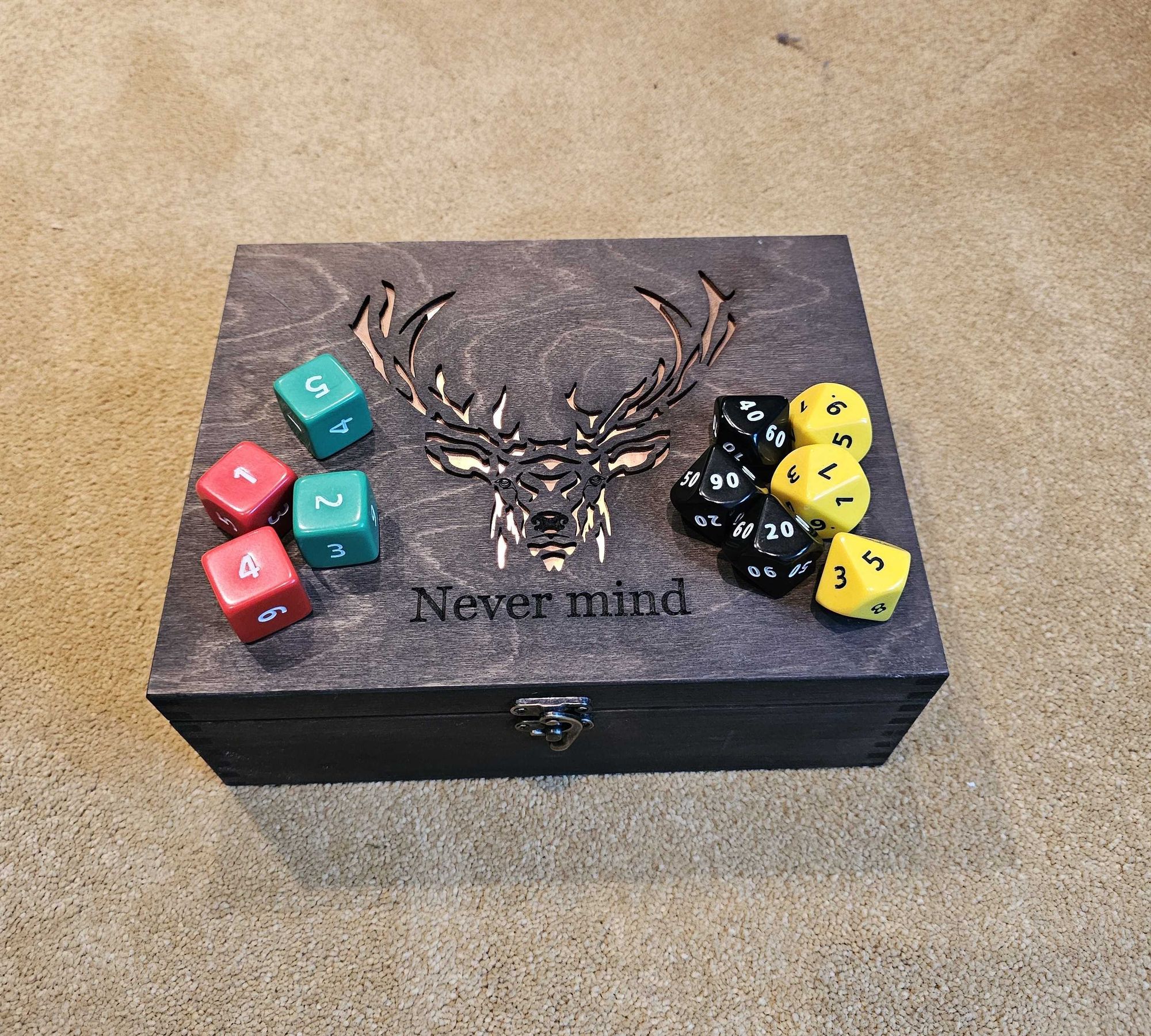 A set of large d6 and percentile dice on a dice box with an engraving of a deer and the word nevermind written on it.