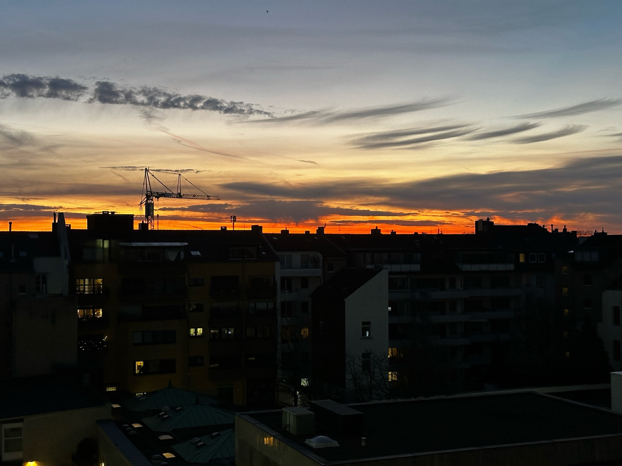 Die Silhouette der nächtelichen Stadt. Darüber ein Streifen oranges Glühen der aufgehenden Sonne