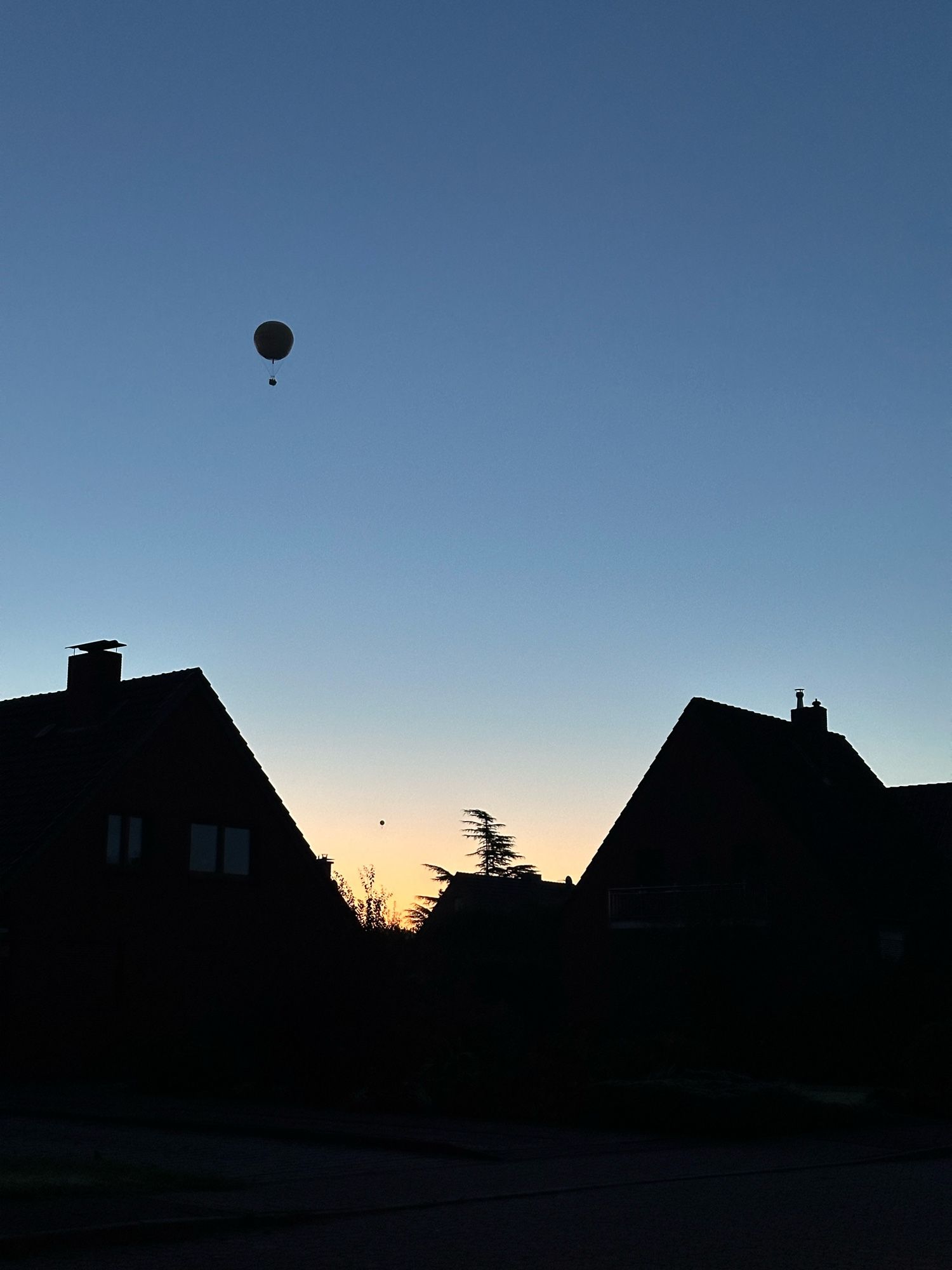 Zwischen Häusern geht die Sonne auf, darüber schwebt ein großer Ballon