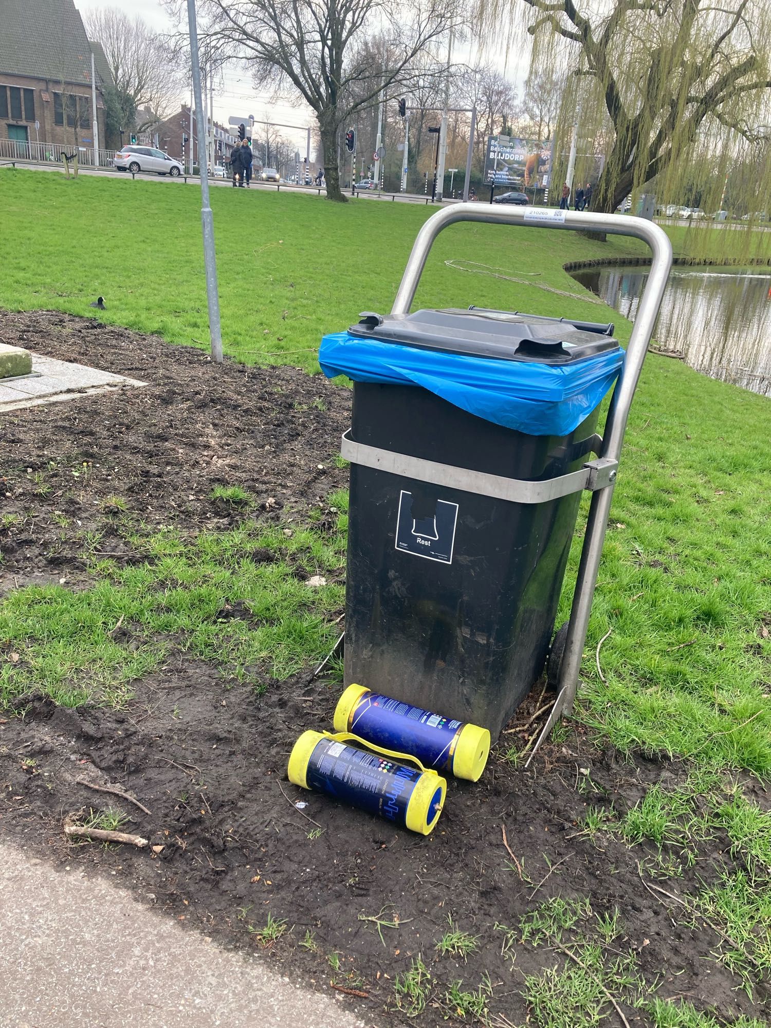 Vuilcontainer met blauwe zak en daarvoor liggen 2 gele lege lachgas cilinders.